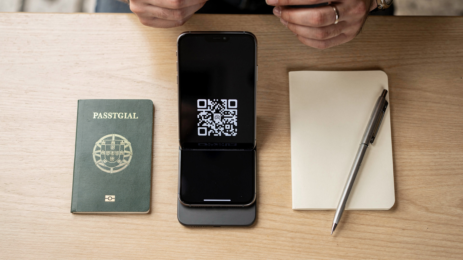 Uma vista aérea de uma mesa de café minimalista, com um smartphone exibindo um QR code de eSIM sendo escaneado por outro smartphone, ao lado de um passaporte e um bloco de notas, em um café tranquilo no bairro de Baixa, em Lisboa.