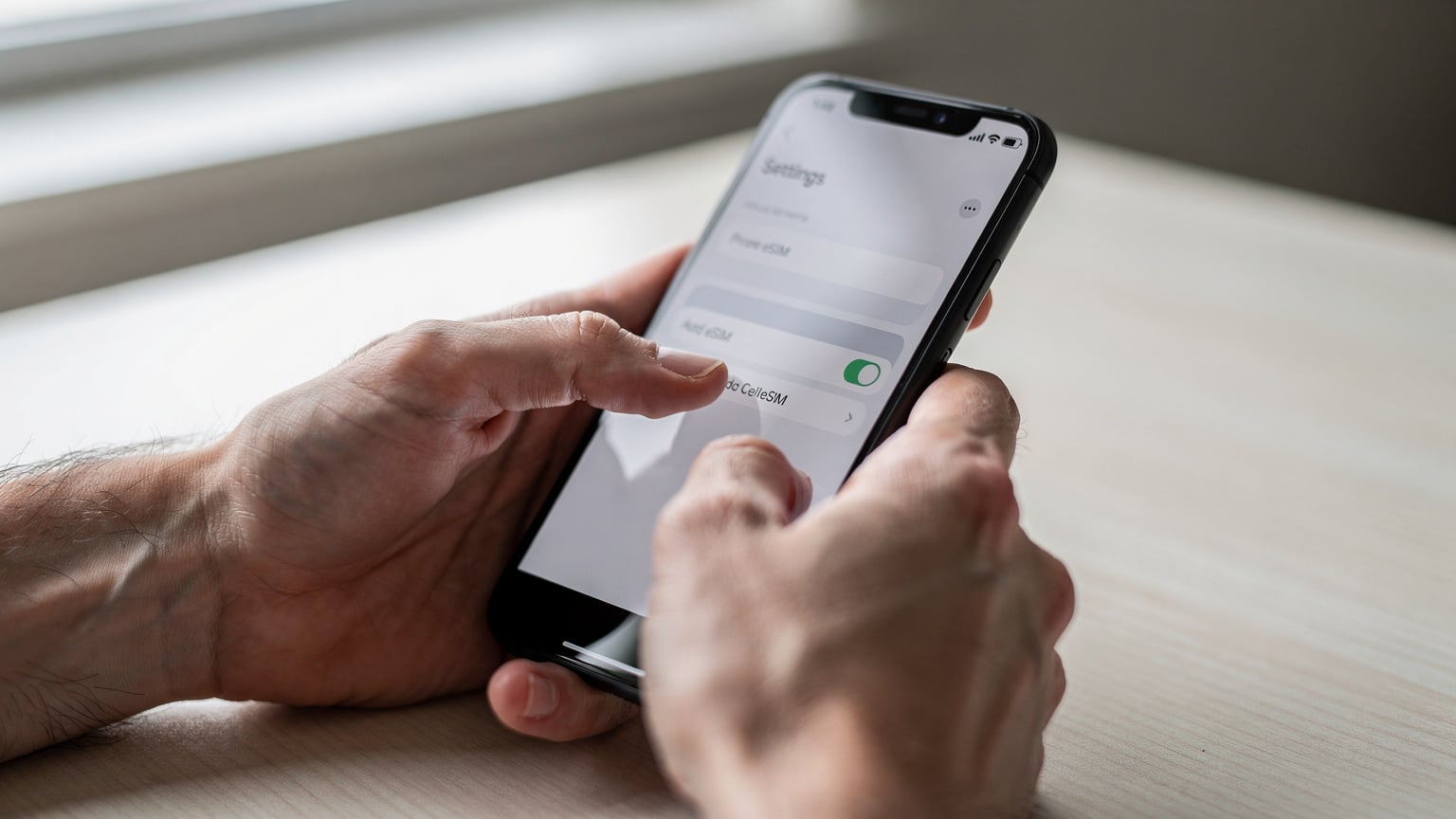 Human hands, one holding a smartphone and the other gently tapping the 'Add eSIM' option within a phone's settings menu, illustrating the activation process.