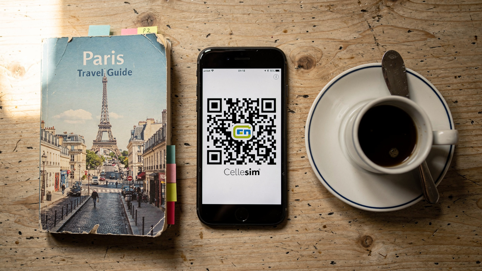 Ein Smartphone zeigt einen Cellesim eSIM QR-Code, daneben liegen ein Reiseführer und eine französische Kaffeetasse auf einem Holztisch.