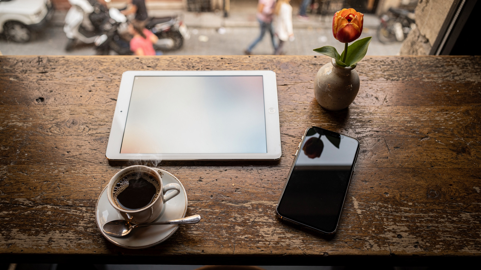 Bir kafenin penceresinden görünen İstanbul'un hareketli bir caddesinde, bir tablet ve kahve yanında bir akıllı telefonun ekranında eSIM sağlayıcılarının karşılaştırma tablosu açık duruyor.