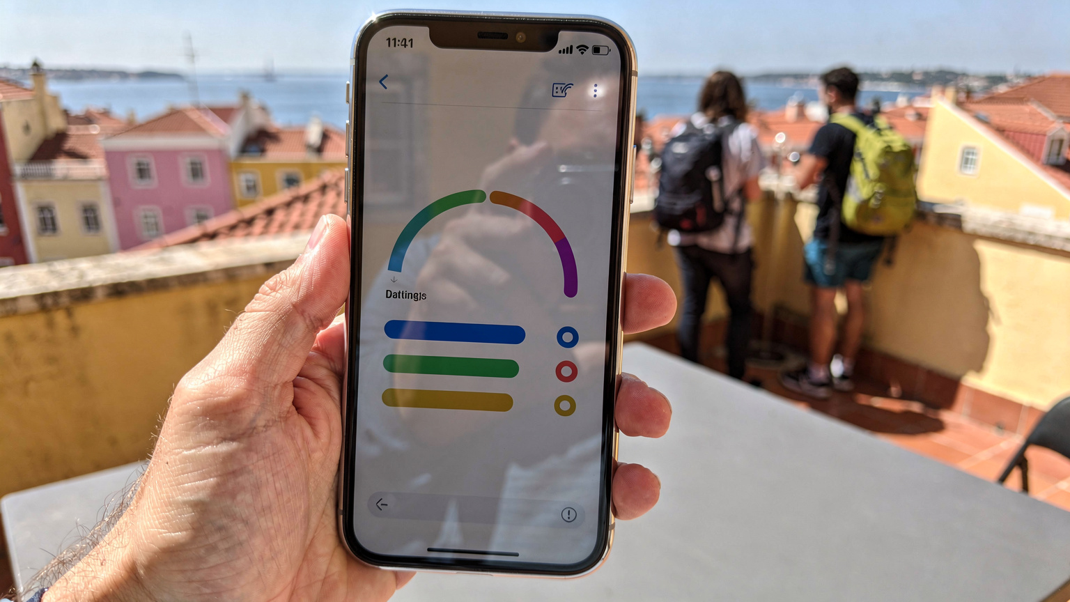 Un primo piano di uno smartphone che mostra l'interfaccia dell'app Cellesim, con il grafico del consumo dati ben visibile e un saldo residuo. Sullo sfondo, una terrazza di un ostello a Lisbona.