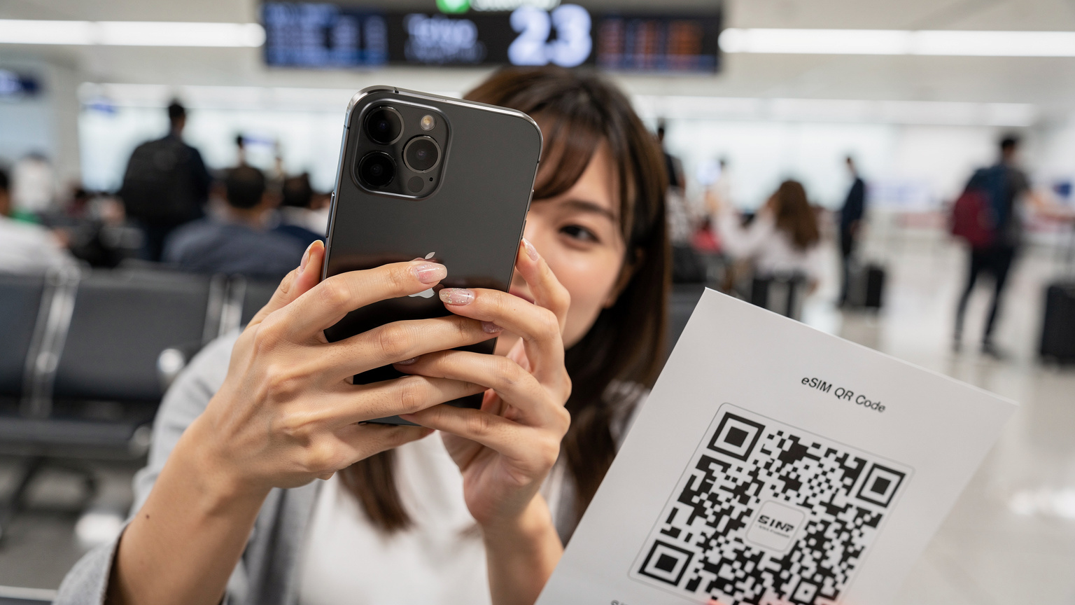 空港の搭乗ゲートで、慌ててeSIMのQRコードをスキャンしている女性の手元。彼女のiPhone 15 Pro Maxが鮮明に写り、背景には出発を待つ人々がぼやけている。
