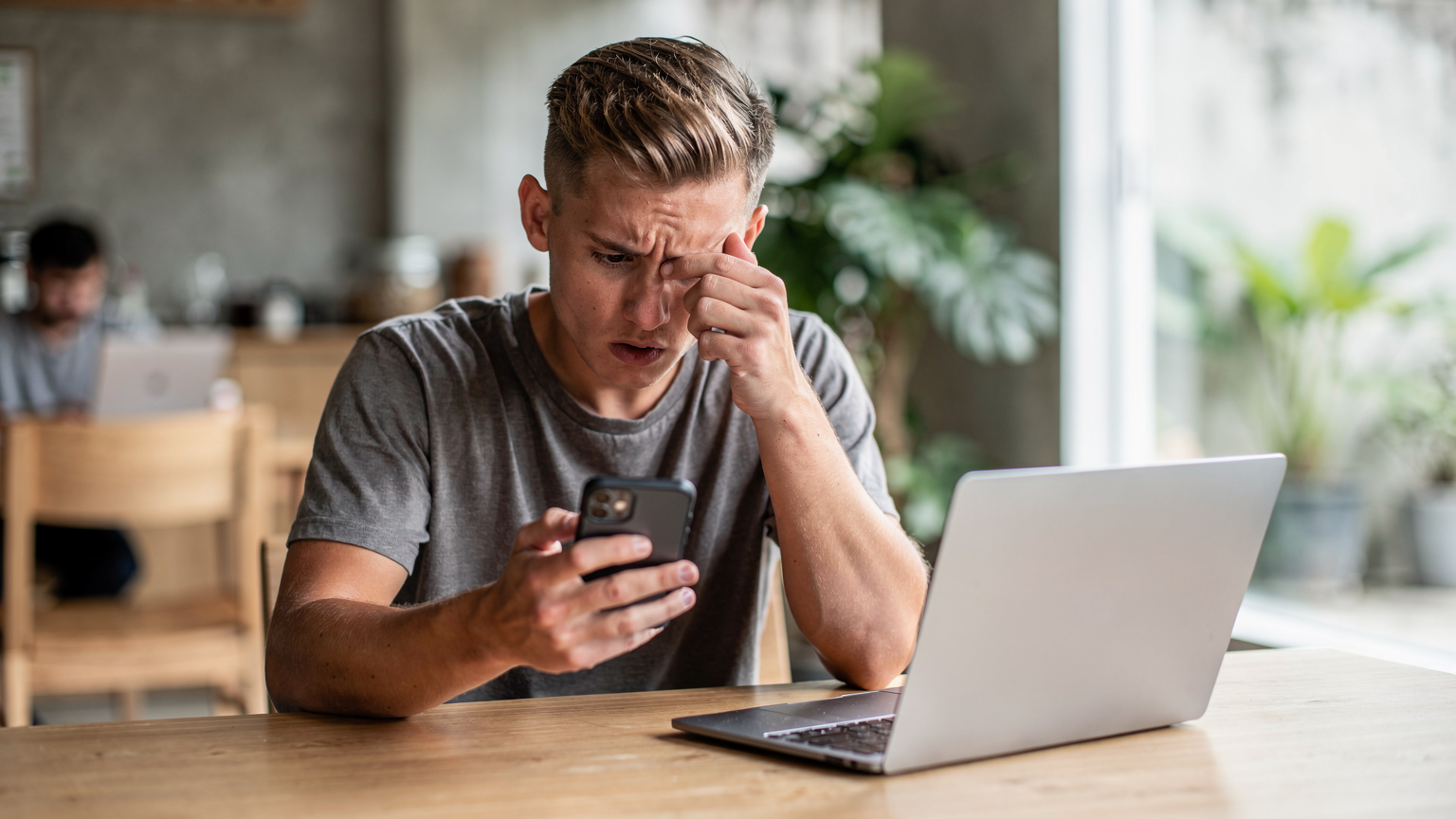 A digital nomad in a co-working space in Canggu, Bali, looking frustrated at their smartphone, which displays a 'No Service' or 'Limited Connectivity' message, with a laptop open nearby.