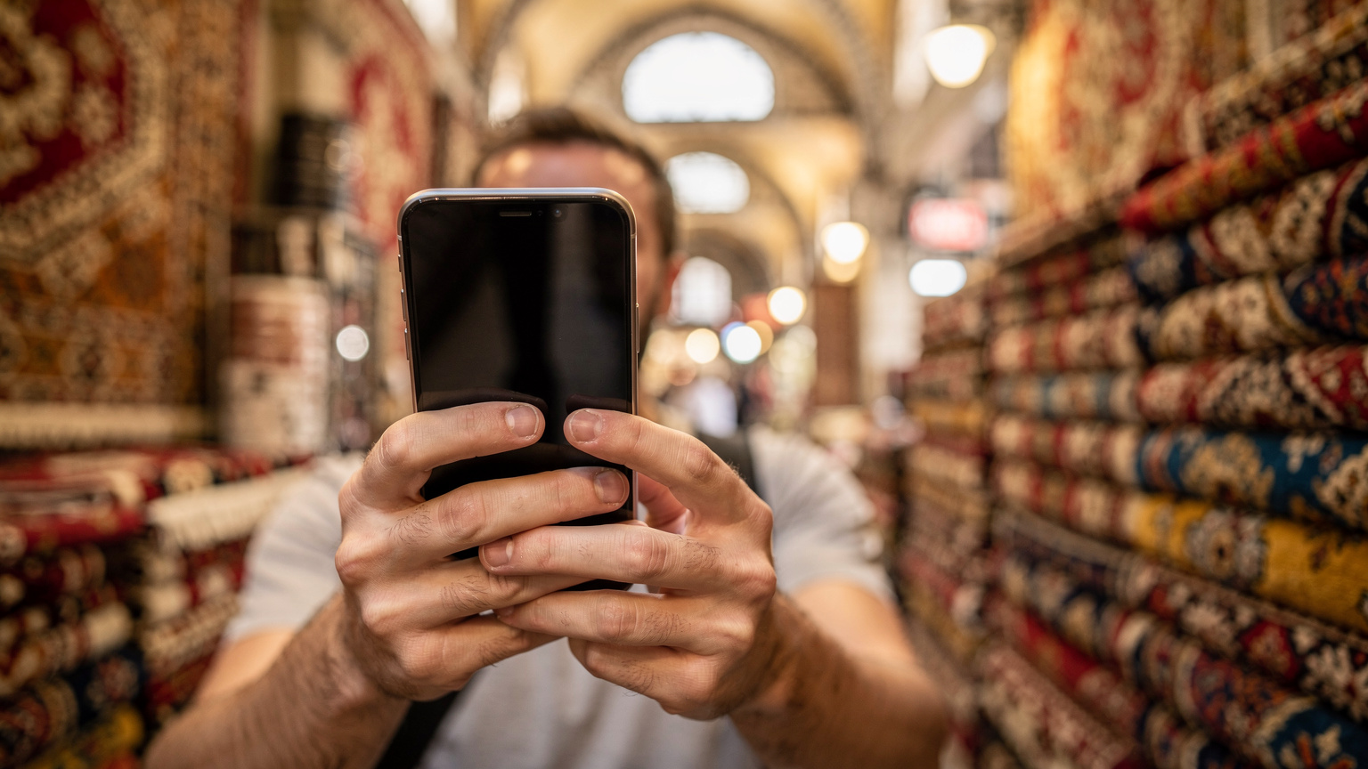 A traveler in Istanbul's Grand Bazaar carefully comparing eSIM plans on their smartphone, with vibrant textiles in the background.