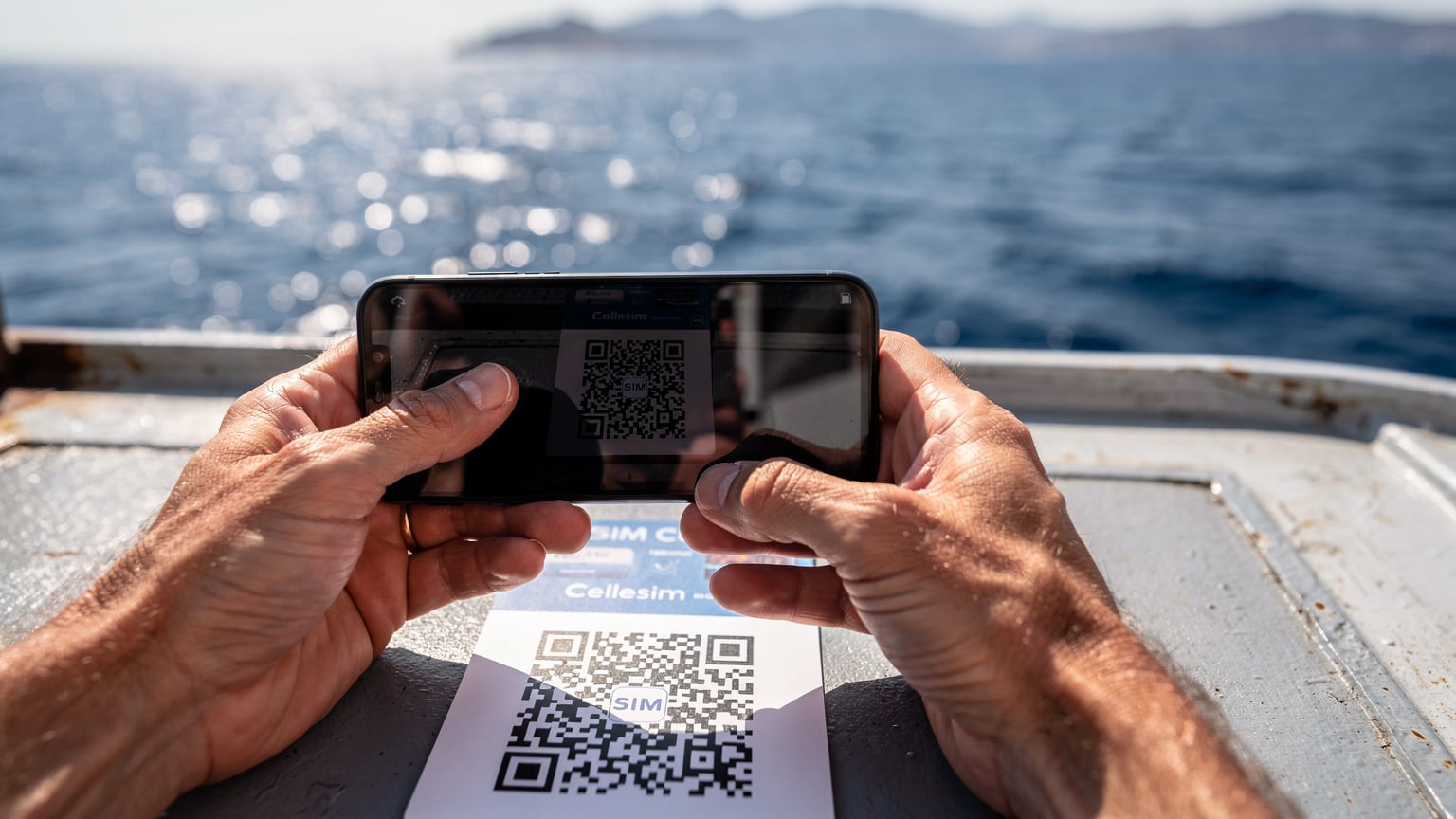 Bir gezgin, feribotta telefonunu kullanarak Cellesim uygulamasından eSIM kurulumu için QR kodunu tarıyor, etrafında Ege Denizi'nin manzarası var.