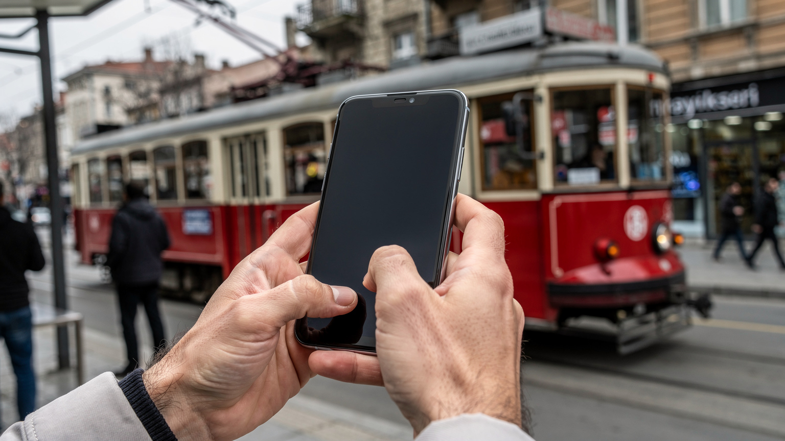 Bir seyahat eden, İstanbul'daki bir otobüs durağında elindeki akıllı telefondan eSIM kurulumu için QR kodu tarıyor, arkada tarihi bir tramvay geçiyor.