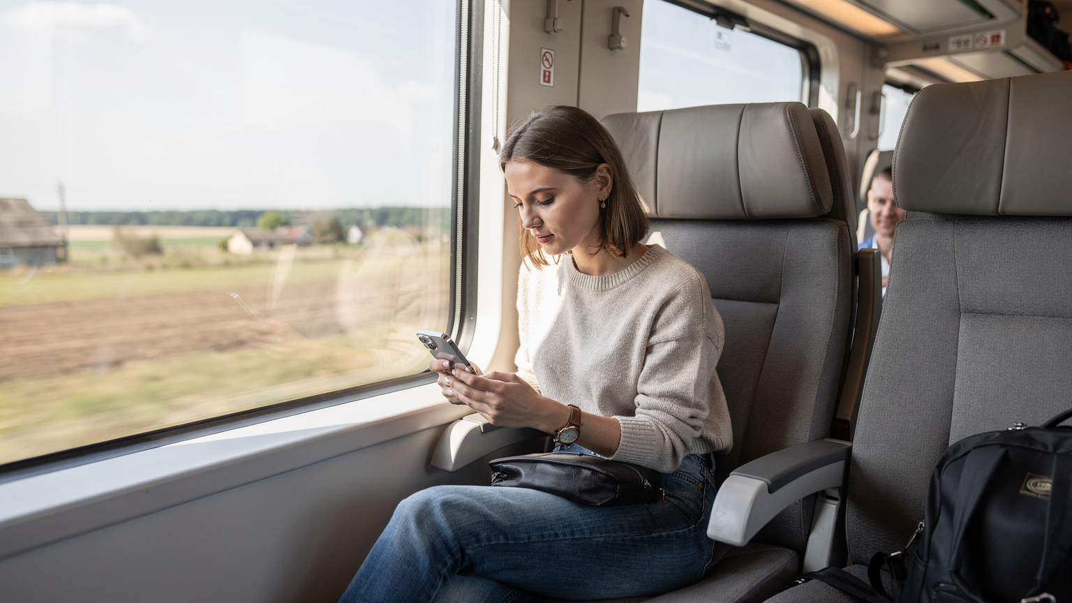 Жінка з iPhone 17 у руці, сидячи у вагоні поїзда Intercity+ в Україні, використовує місцевий Wi-Fi, демонструючи розумне управління даними під час подорожі.
