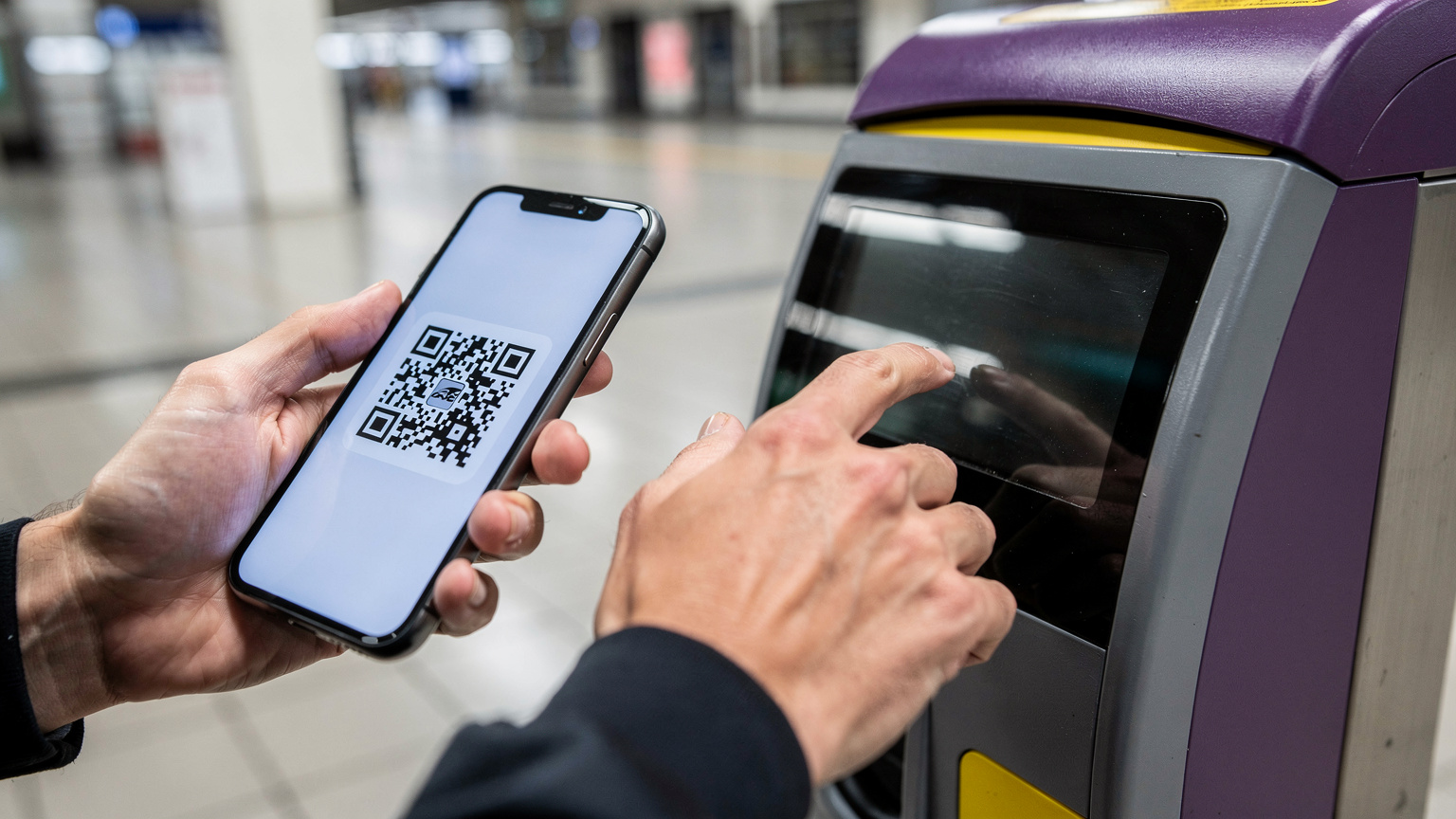 Manos de un viajero utilizando su smartphone para validar un billete en una máquina expendedora de la SNCF.