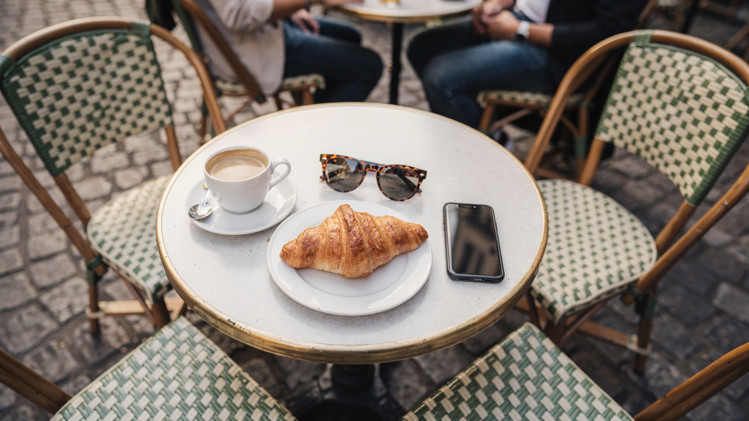 Personas disfrutando de café y la atmósfera en la terraza de una cafetería parisina, con un smartphone sobre la mesa.