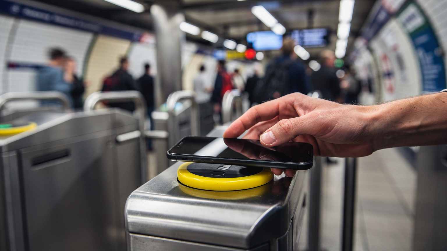 Close-up of a hand tapping a smartphone on a contactless payment reader at a London Underground gate, showing the ease of transit payment.