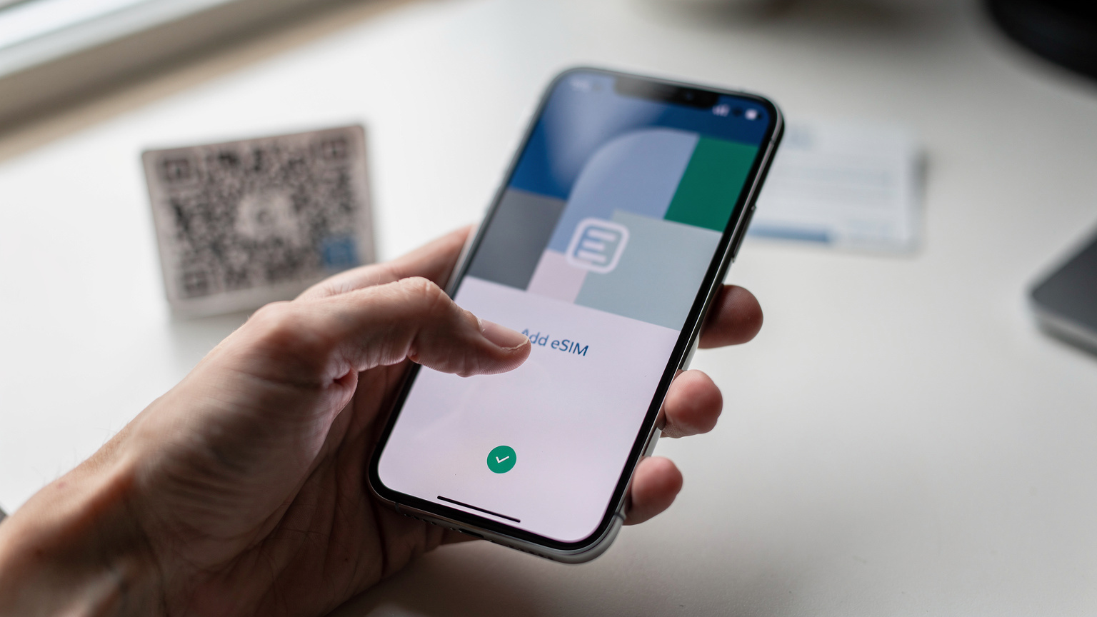 Nærbilde av en hånd som holder en smarttelefon, med fokus på skjermen som viser innstillingene for eSIM-aktivering, muligens en QR-kode eller et felt for manuell inntasting.