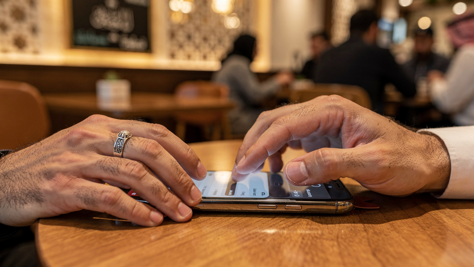 أيدي تضبط إعدادات الشبكة على هاتف ذكي، مع التركيز على خيارات شريحة eSIM، في خلفية غير واضحة لمقهى مزدحم.