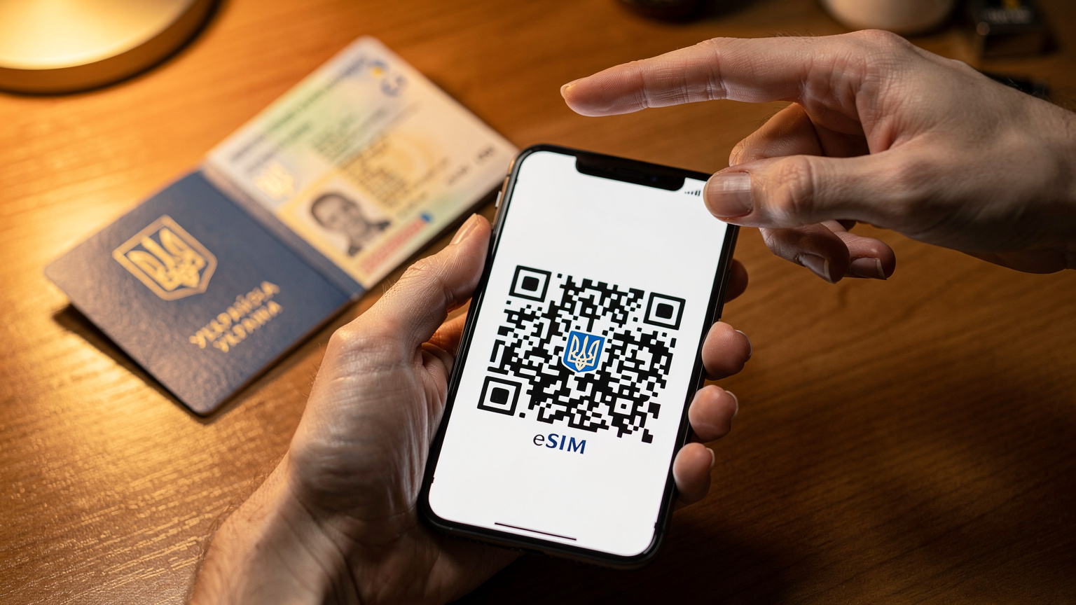 Крупний план рук, які тримають смартфон, на екрані якого відображається процес сканування QR-коду для активації eSIM. На фоні лежить український паспорт.