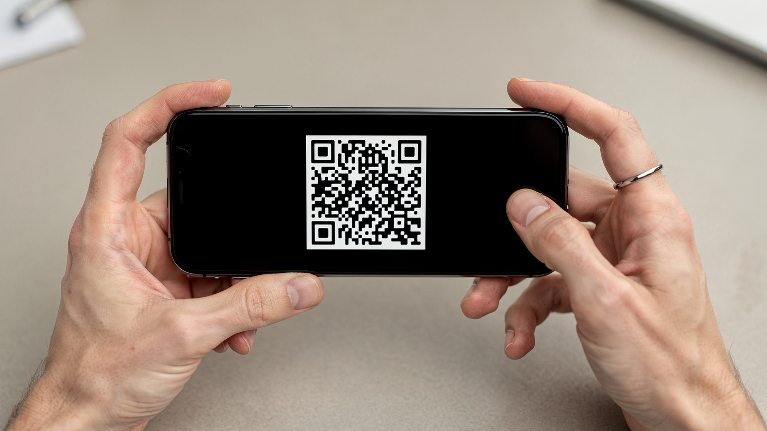 Zblízka záber na ľudské ruky držiace smartfón, na obrazovke je zobrazený QR kód, ktorý sa chystajú naskenovať.