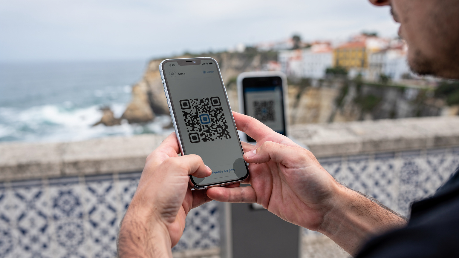 Mãos de uma pessoa a digitalizar um código QR num smartphone para ativar um eSIM, com uma paisagem costeira de Portugal desfocada ao fundo, transmitindo facilidade e liberdade.
