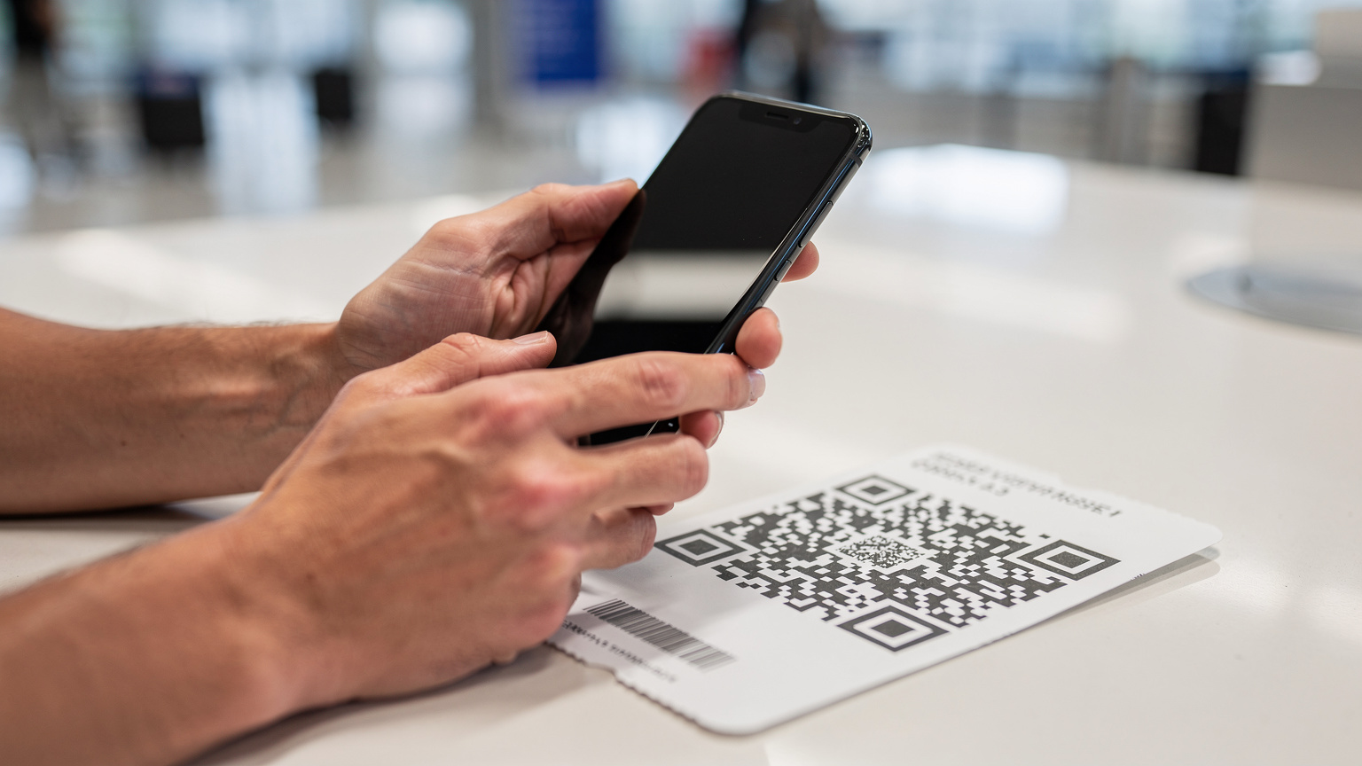 Gros plan sur les mains d'un voyageur utilisant son smartphone pour scanner un QR code d'activation eSIM, sur un comptoir d'aéroport ou de gare.