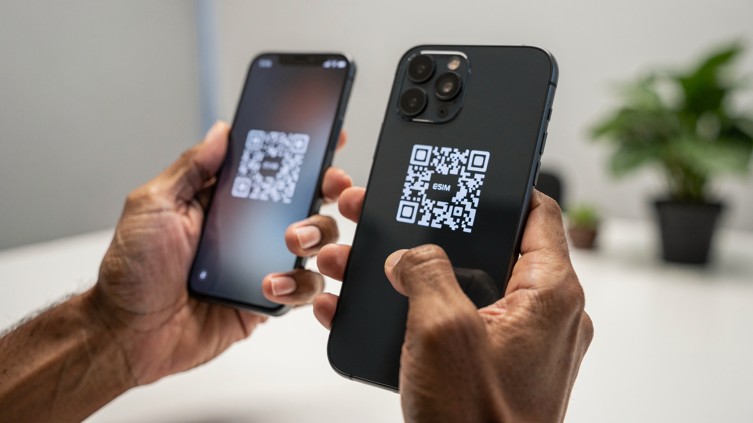 Een close-up van handen die een QR-code scannen op een smartphone, waarbij de focus ligt op de interactie tussen de twee apparaten. De achtergrond toont subtiel een modern kantoorinterieur met planten.