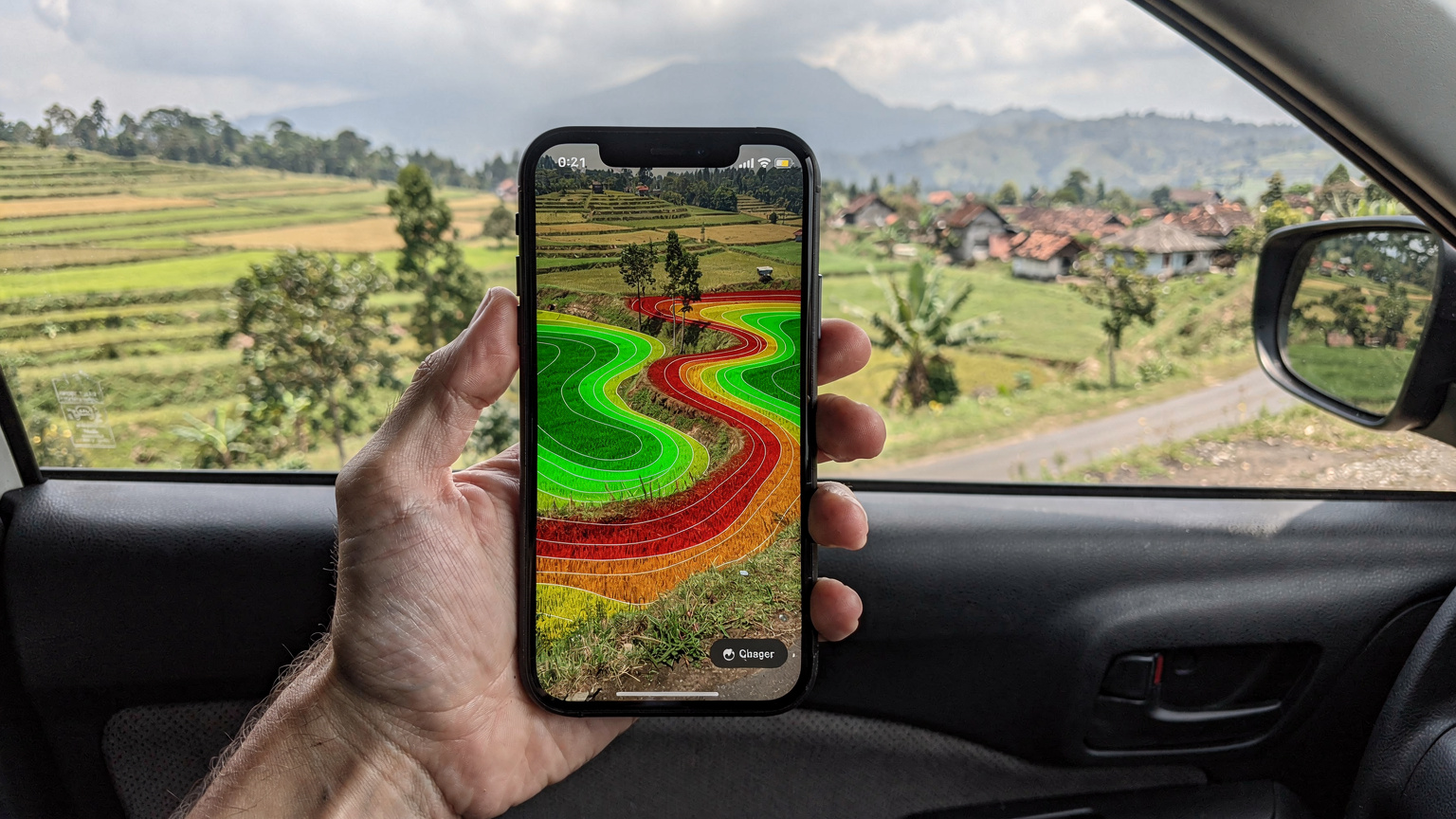 Tangan seorang pria memegang ponsel yang menampilkan aplikasi peta cakupan jaringan dengan warna-warni yang menunjukkan titik-titik sinyal kuat dan lemah di area pedesaan Jawa Timur, dengan fokus pada tantangan konektivitas.