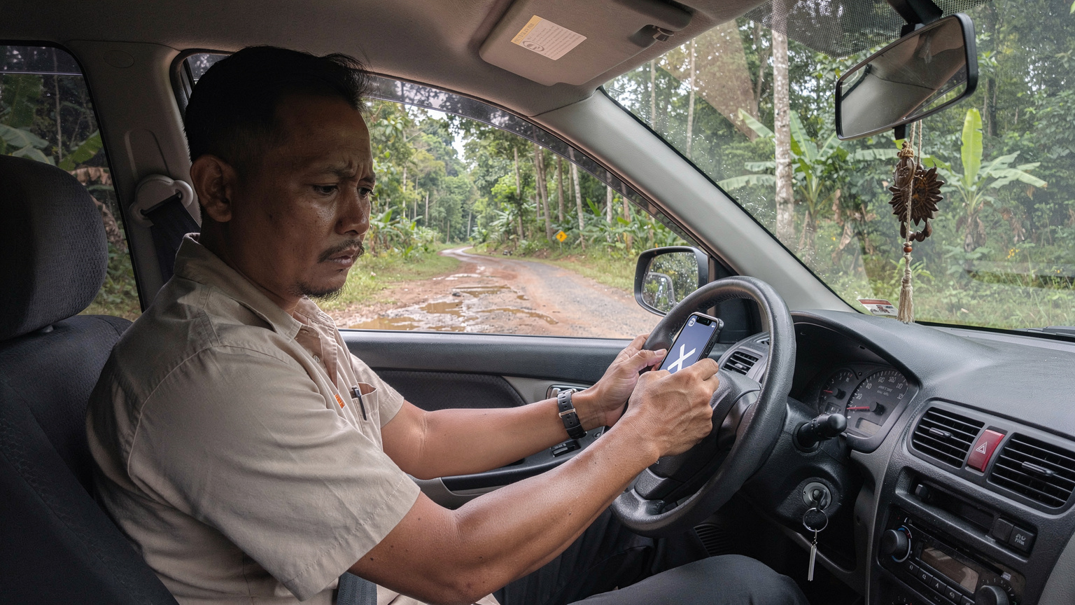 Seorang pengemudi dengan ekspresi cemas melihat ponselnya yang menunjukkan 'No Service' di layar, saat mobilnya berhenti di pinggir jalan yang sepi di tengah hutan, menunjukkan frustrasi dengan konektivitas yang buruk.