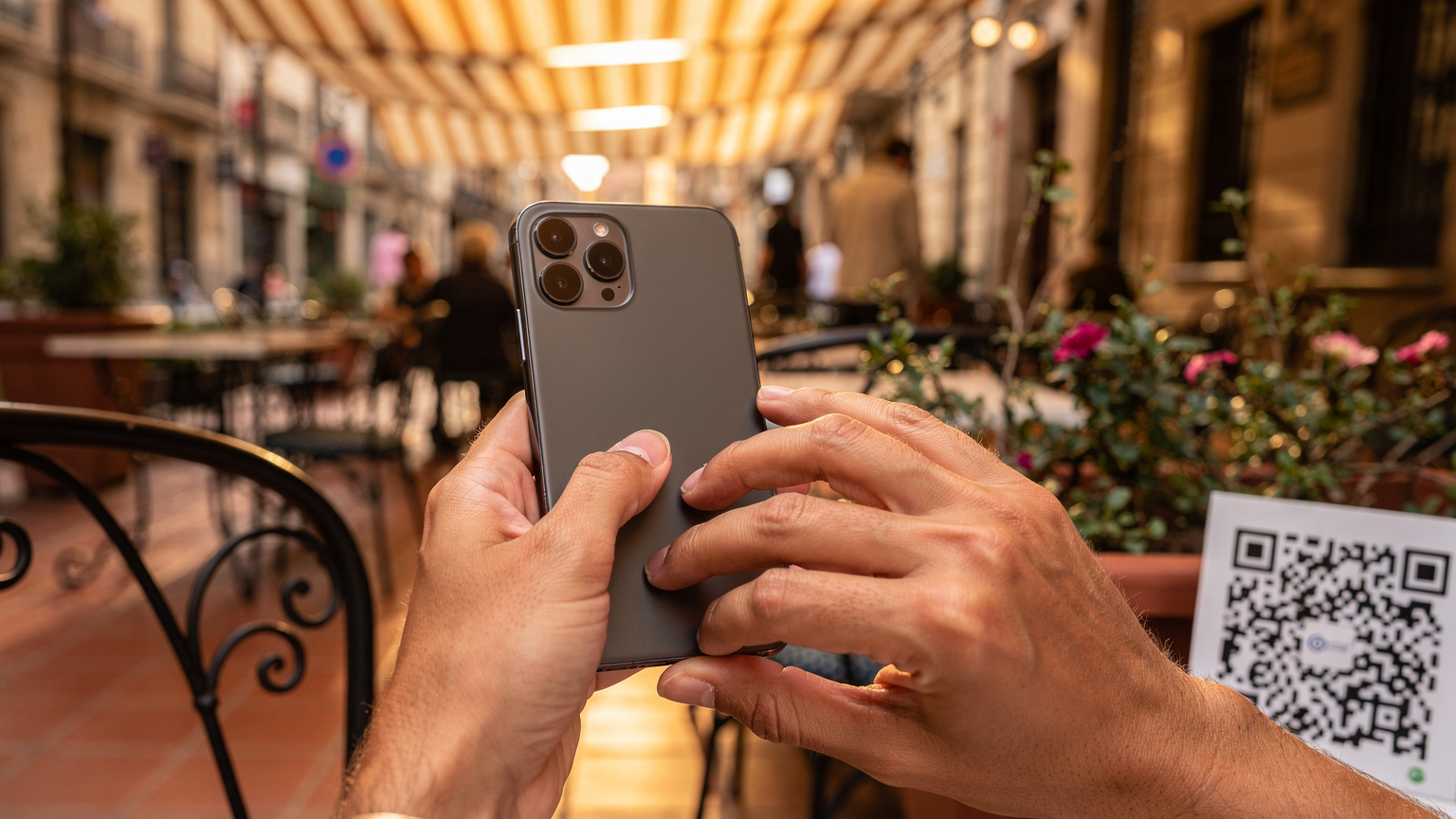 A close-up shot of a traveler's hands holding a smartphone, scanning a QR code displayed on another device or a printed paper, against a blurred background of a vibrant, sun-drenched street cafe in Valencia, Spain.