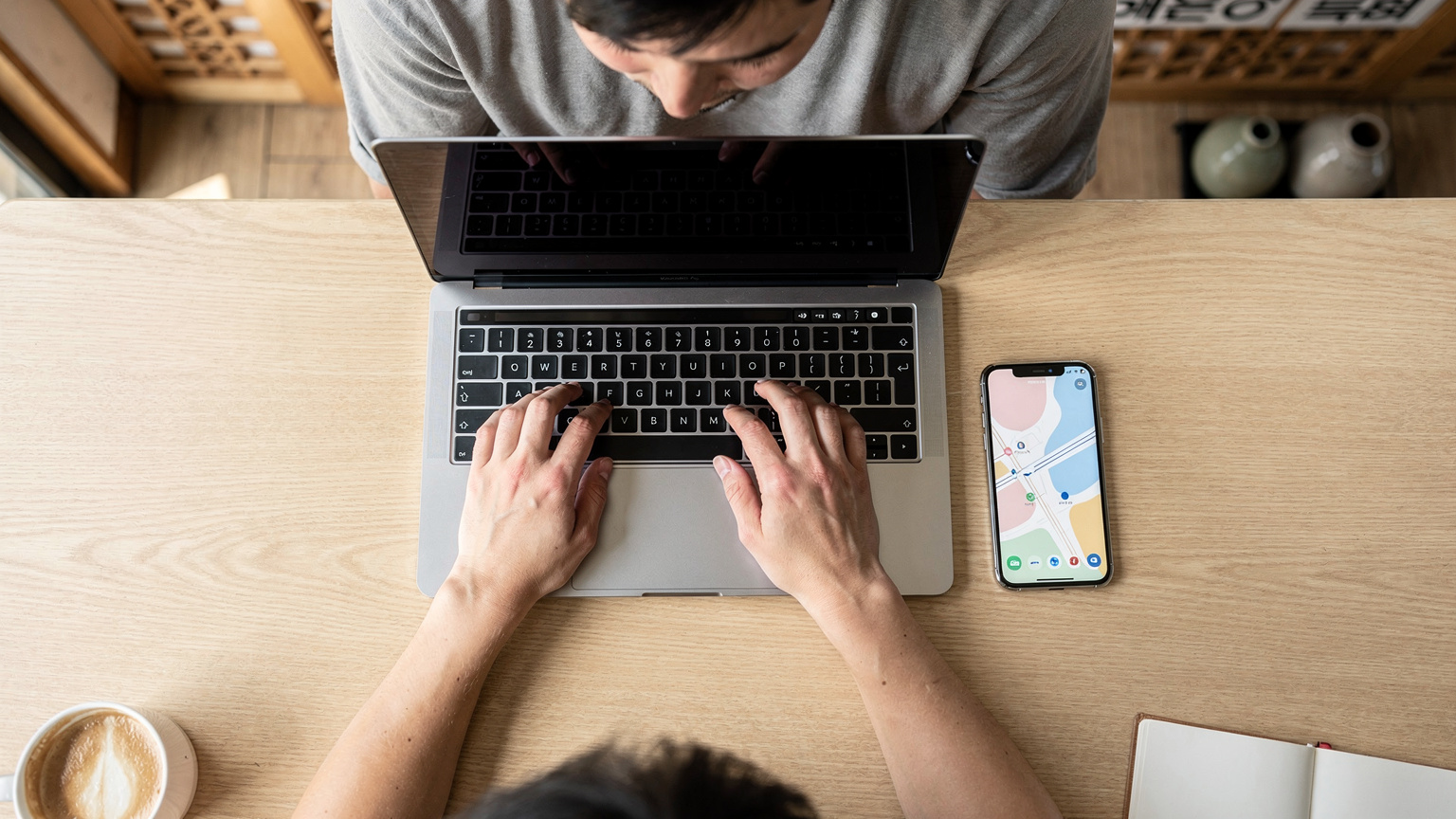 A digital nomad's hands typing on a sleek laptop, with a smartphone displaying a map application next to it on a minimalist wooden cafe table in a modern Seoul cafe, emphasizing fast connectivity and remote work.