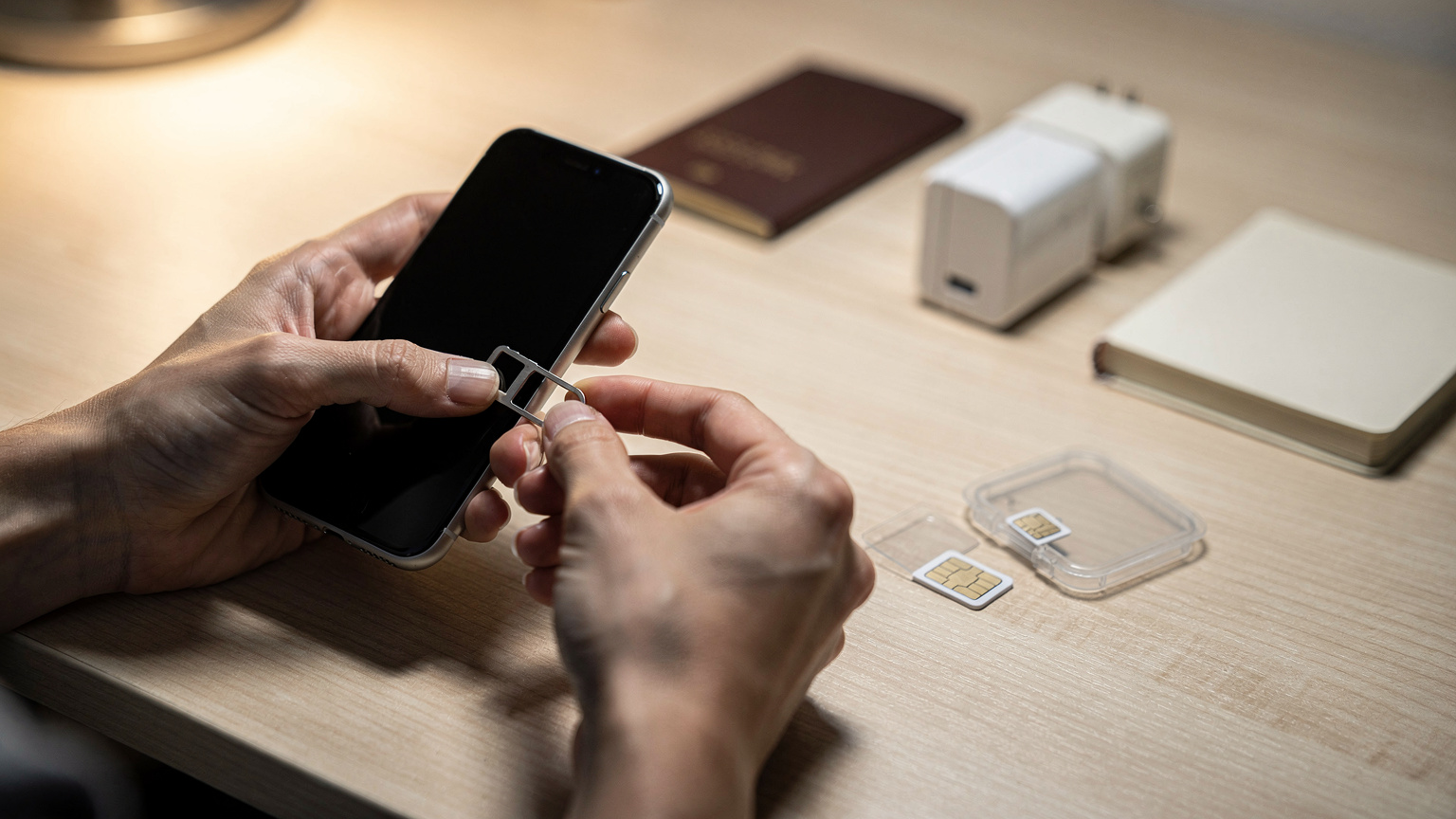 丁寧に物理SIMをiPhoneのSIMトレイから取り出し、小さな保護ケースに保管する旅行者の手元。背景は旅立ち前の整頓されたデスク。
