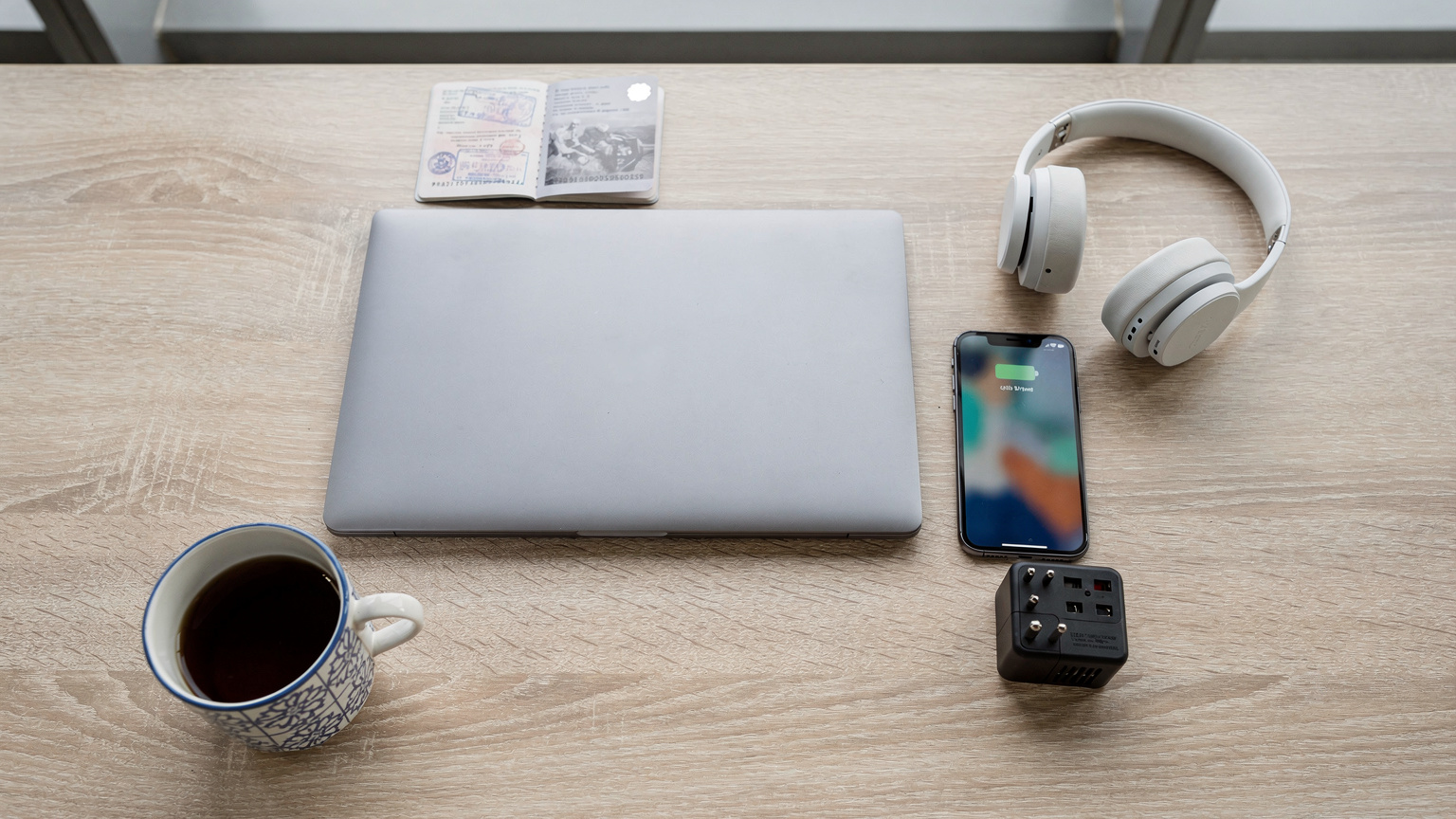 An overhead flat-lay of a digital nomad's desk in a co-working space, featuring a laptop, a smartphone displaying a map, a passport, a travel adapter, and a local coffee cup. The scene is well-organized and functional.