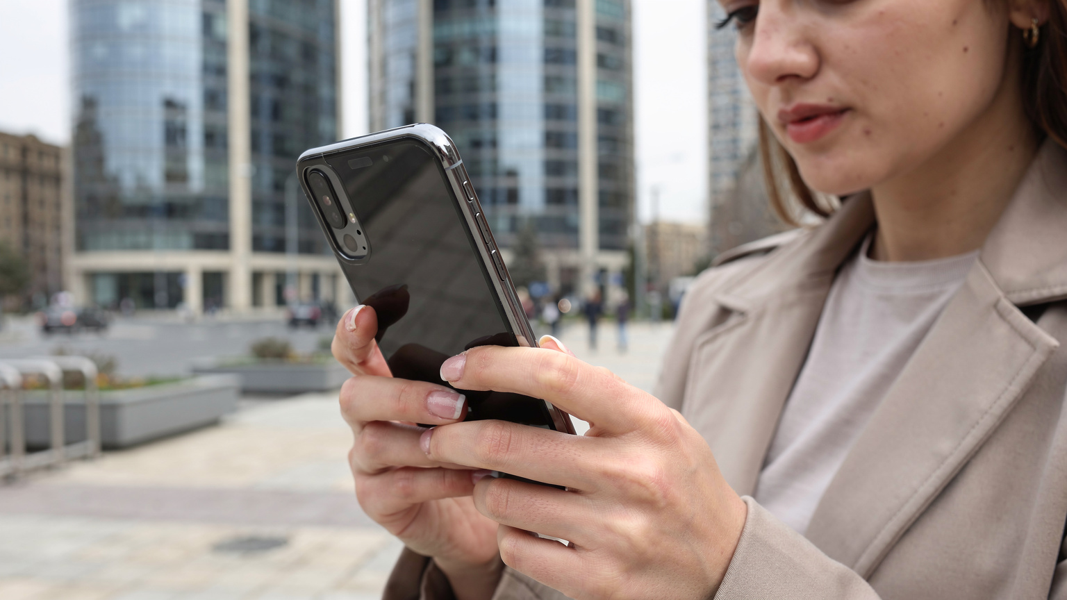 A woman confidently using her smartphone to navigate a map application while exploring the modern streets of Baku, Azerbaijan.