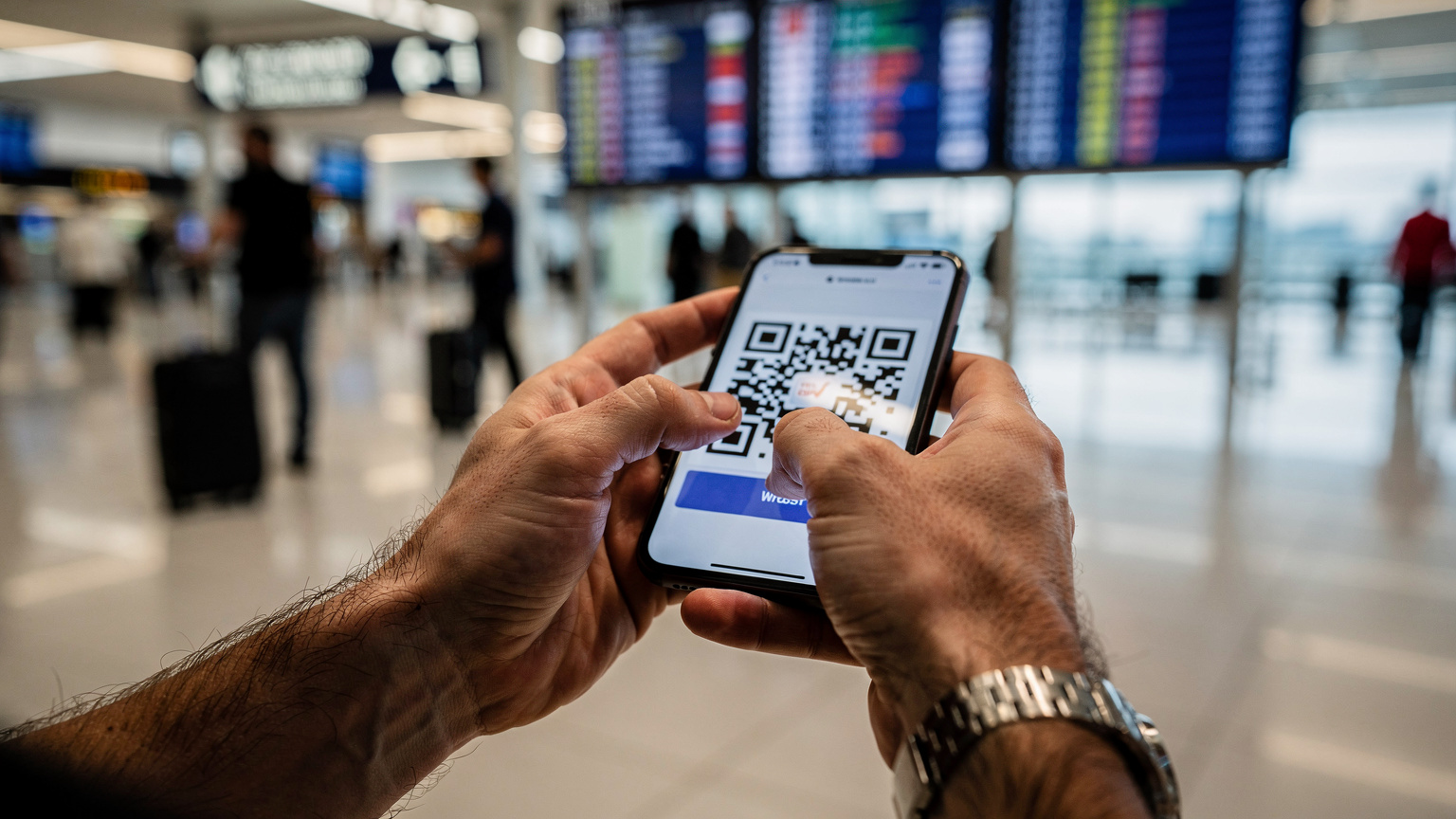 Пътуващ телефонен техник настройва eSIM на своя смартфон, докато е на летището в Истанбул, с багаж и табло за заминаващи полети на заден план.