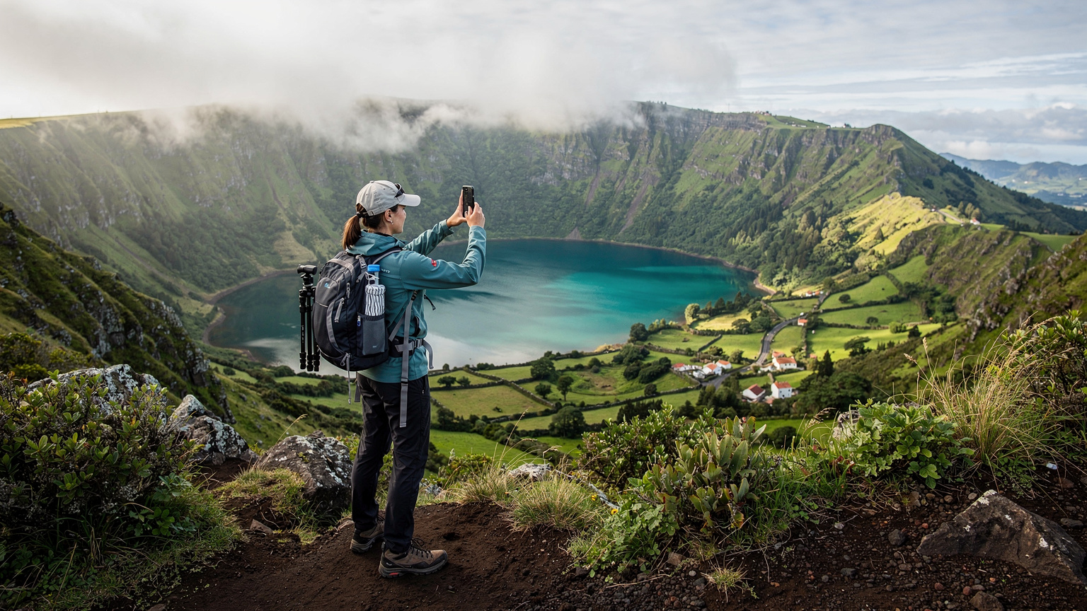 Uma caminhante solitária tira uma foto com seu smartphone enquanto aprecia a vista deslumbrante de um vulcão adormecido nos Açores, Portugal, demonstrando o uso de dados em áreas remotas.