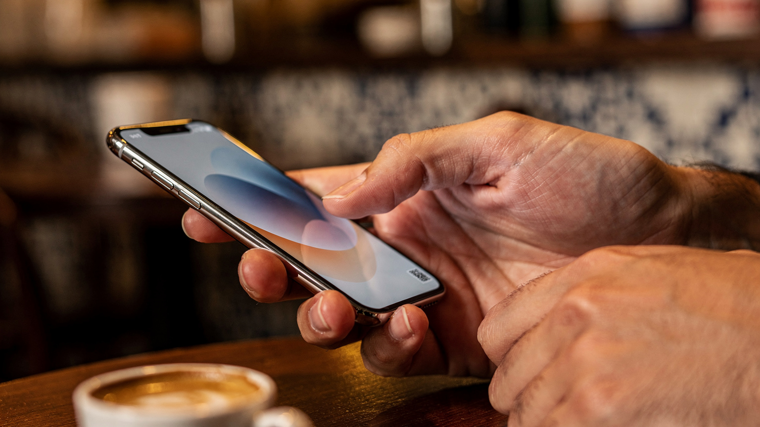 Mãos de uma pessoa segurando um smartphone, com o polegar tocando a tela para instalar um eSIM via QR code, em um café aconchegante em Coimbra, Portugal.