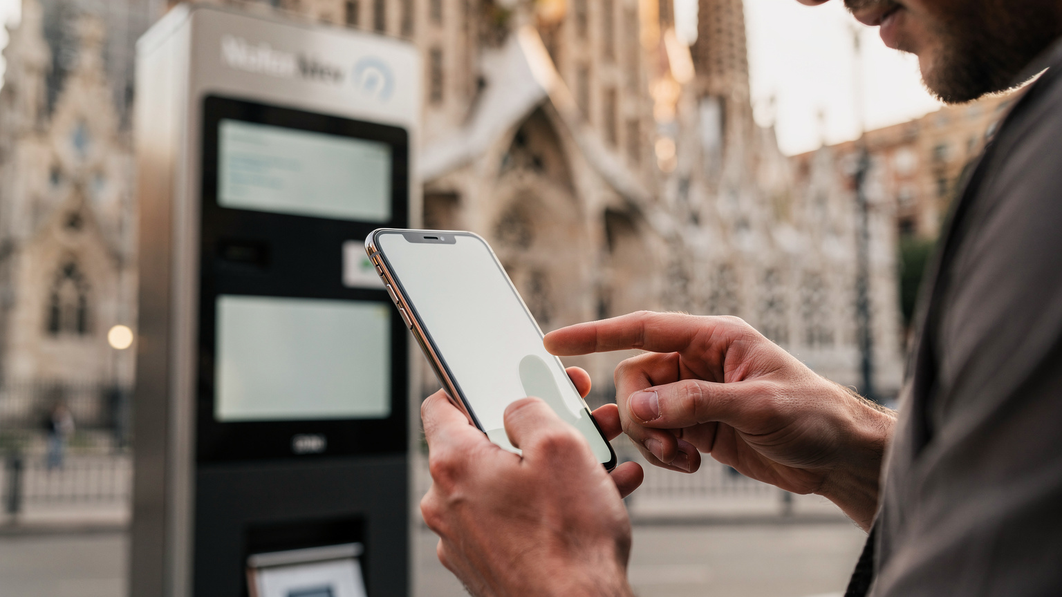 Barselona'da La Sagrada Familia önünde, bir gezgin akıllı telefonunu kullanarak metro bileti satın alıyor. Telefon ekranında dijital bilet arayüzü görünmüyor.