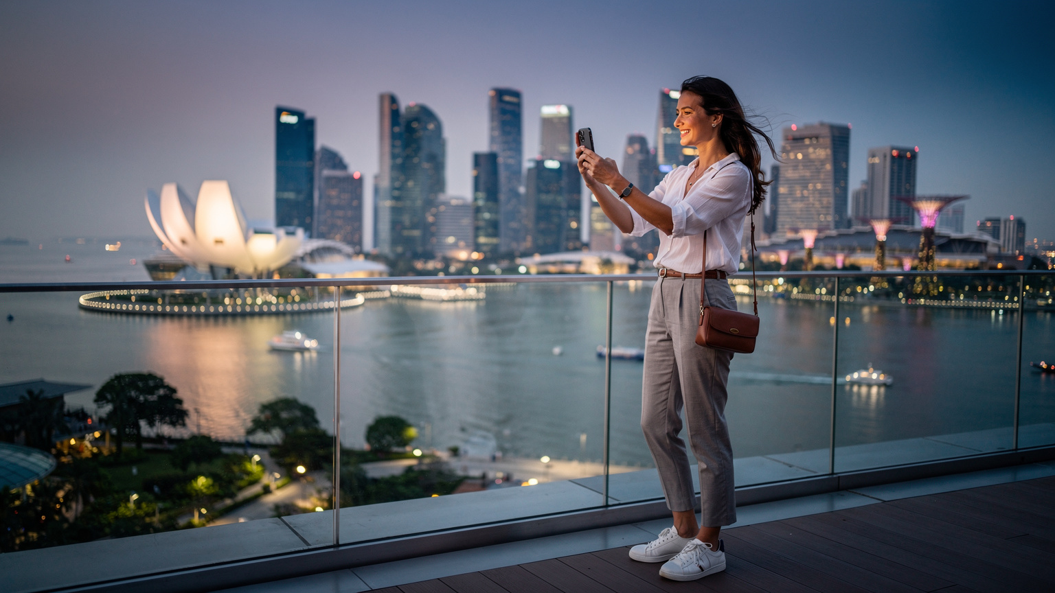 Seorang pengembara sedang menikmati keindahan pemandangan kota Singapura dari Marina Bay Sands, sambil menggunakan telefonnya, mungkin mengambil gambar.