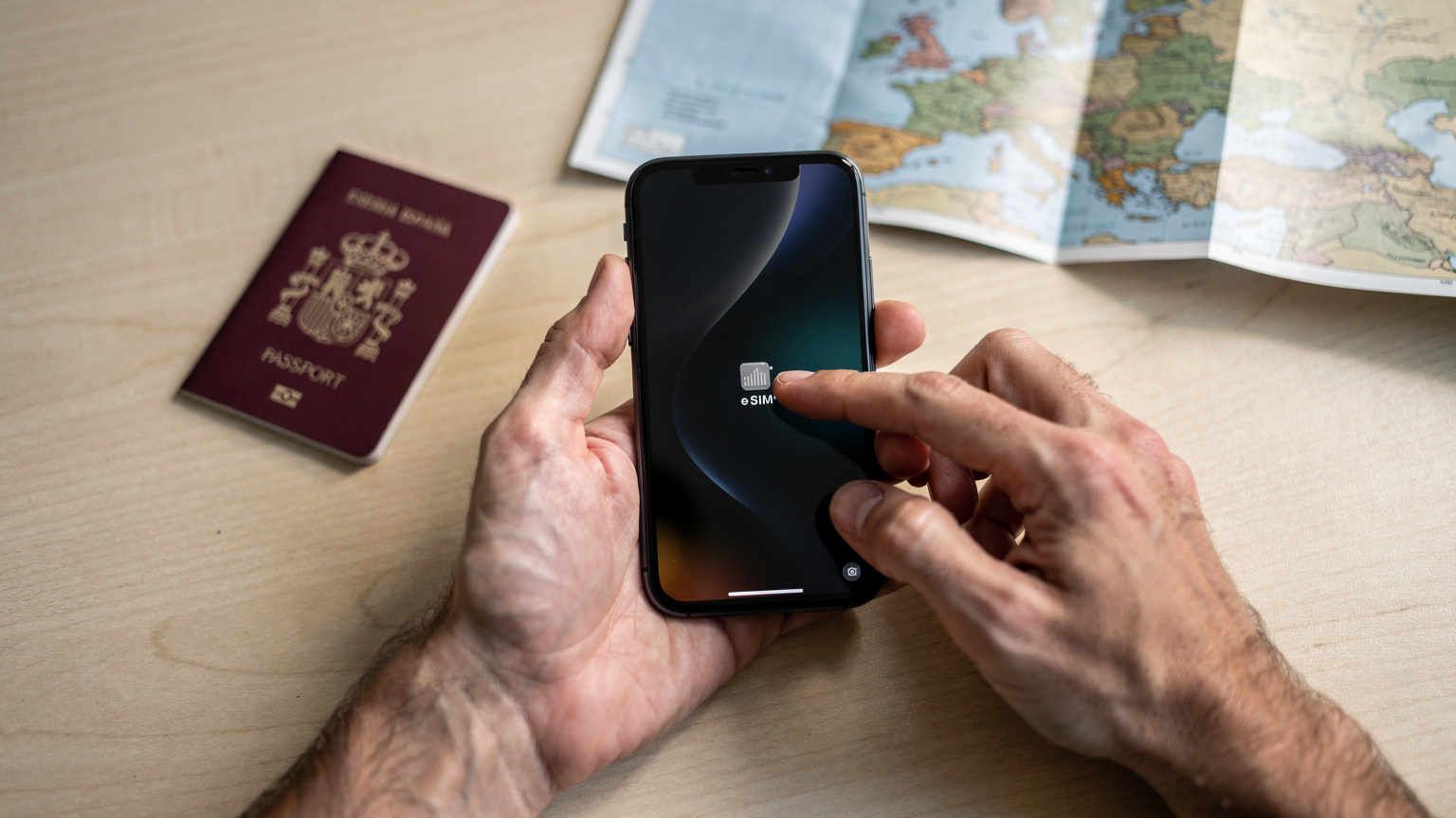 Un hombre activa su eSIM en un smartphone moderno, con un pasaporte y un mapa de Europa en el fondo, antes de un viaje.