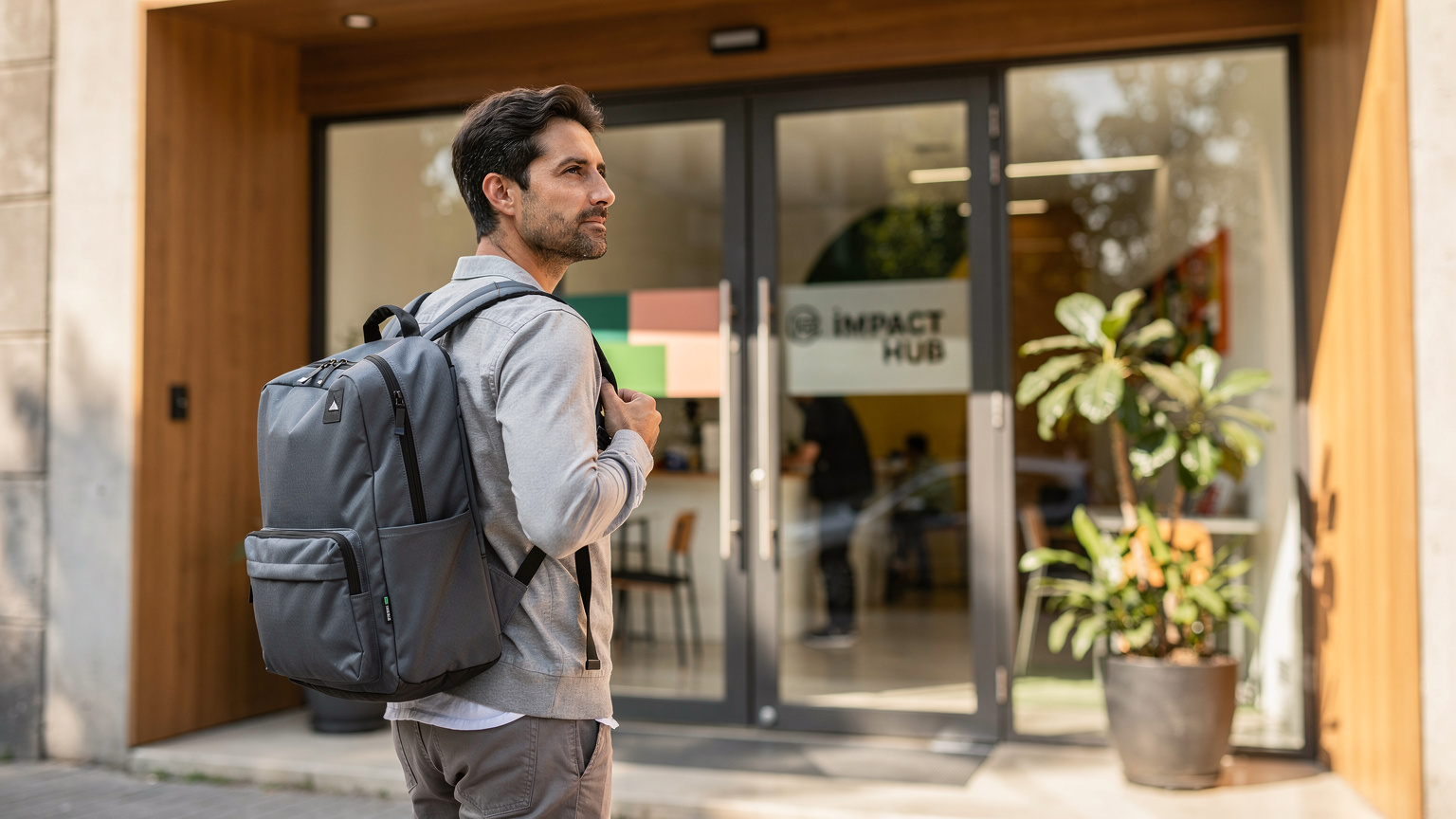 Un nomade digitale con uno zaino ergonomico si trova davanti all'ingresso moderno e accogliente del co-working space 'Impact Hub' a Roma Norte, Città del Messico, pronto per iniziare la giornata lavorativa.