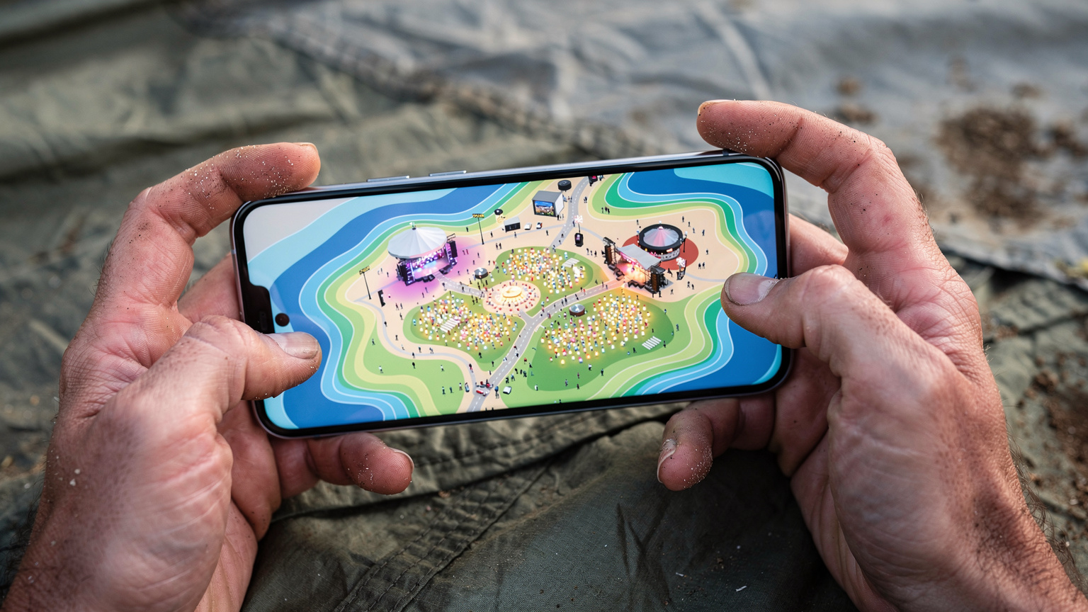 Eine Nahaufnahme von Händen, die ein Smartphone halten, auf dessen Bildschirm eine farbige Netzabdeckungskarte eines imaginären Festivalgeländes mit vielen kleinen, leuchtenden Punkten, die aktive Nutzer darstellen, zu sehen ist.