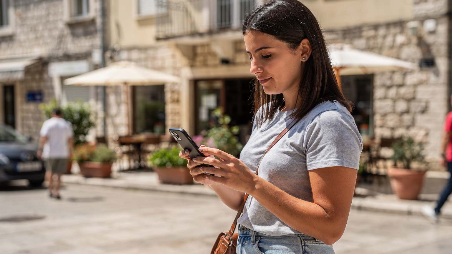 Cestovatelka v Podgorici kontroluje nastavení eSIM na svém telefonu, s pozadím typické černé horynskké ulice a kaváren.