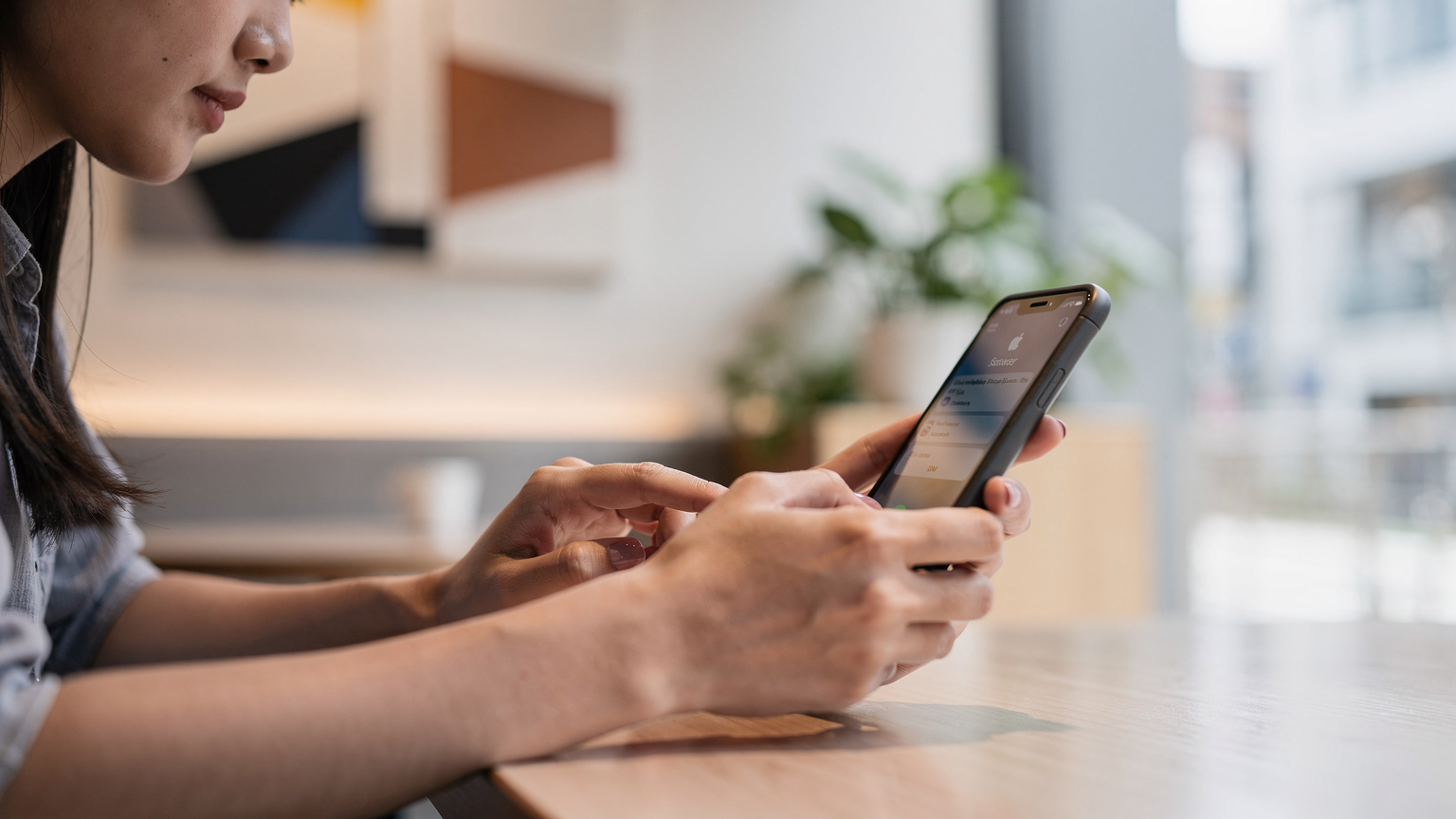 Seorang pengembara muda Malaysia sedang menyemak tetapan iPhone di sebuah kafe moden di Shinjuku, Tokyo, memastikan keserasian eSIM sebelum memulakan hari.