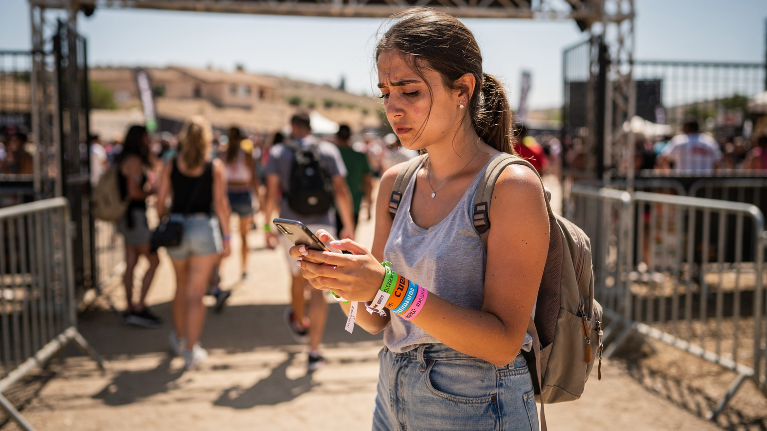 Een festivalganger controleert haar telefoon bij de ingang van een festival, met kleurrijke polsbandjes en een rugzak, terwijl ze probeert verbinding te maken met het netwerk.