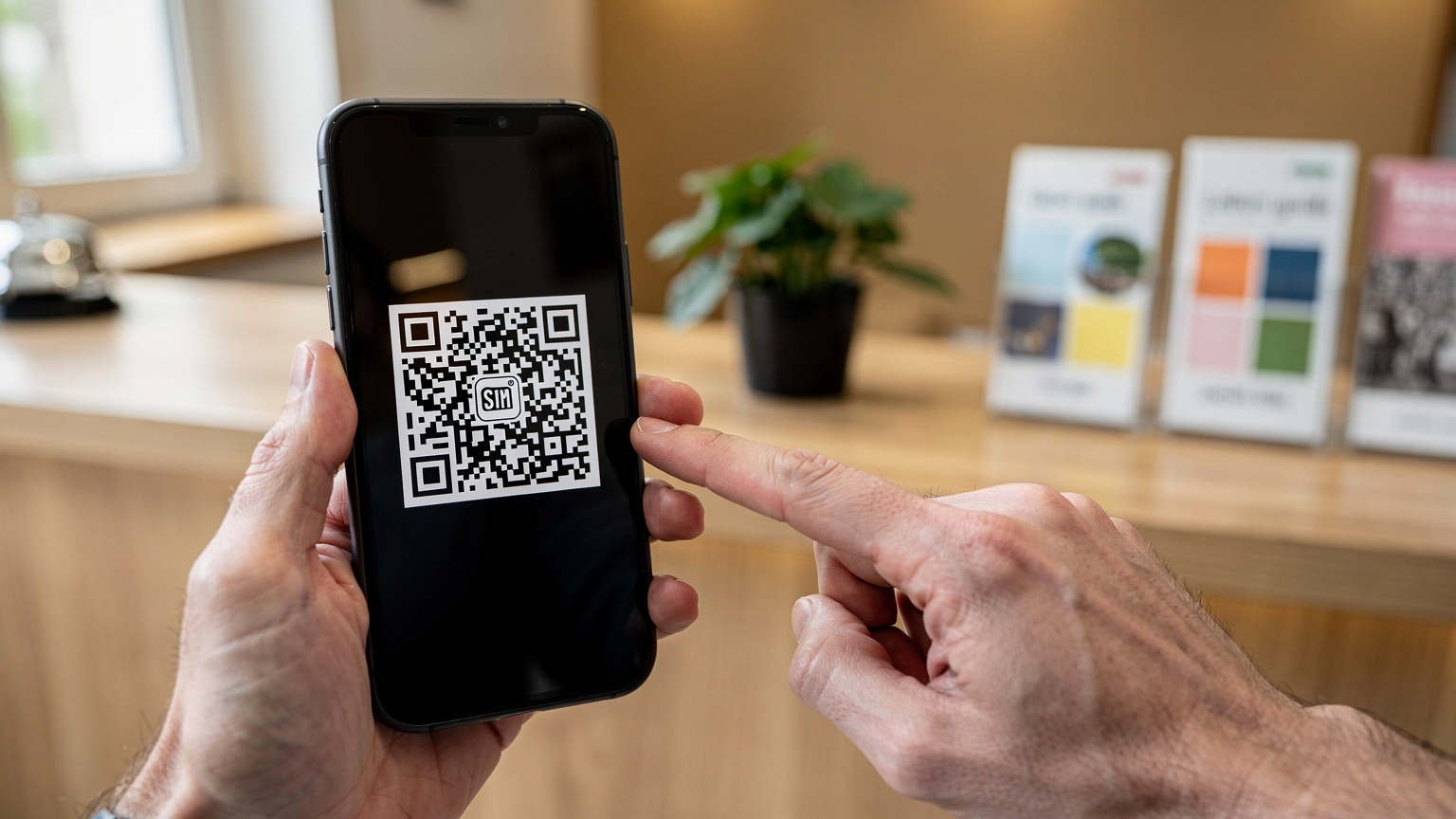 Een close-up van handen die een smartphone vasthouden met een QR-code voor eSIM-activatie, tegen een wazige achtergrond van een hostelreceptie in Lissabon.