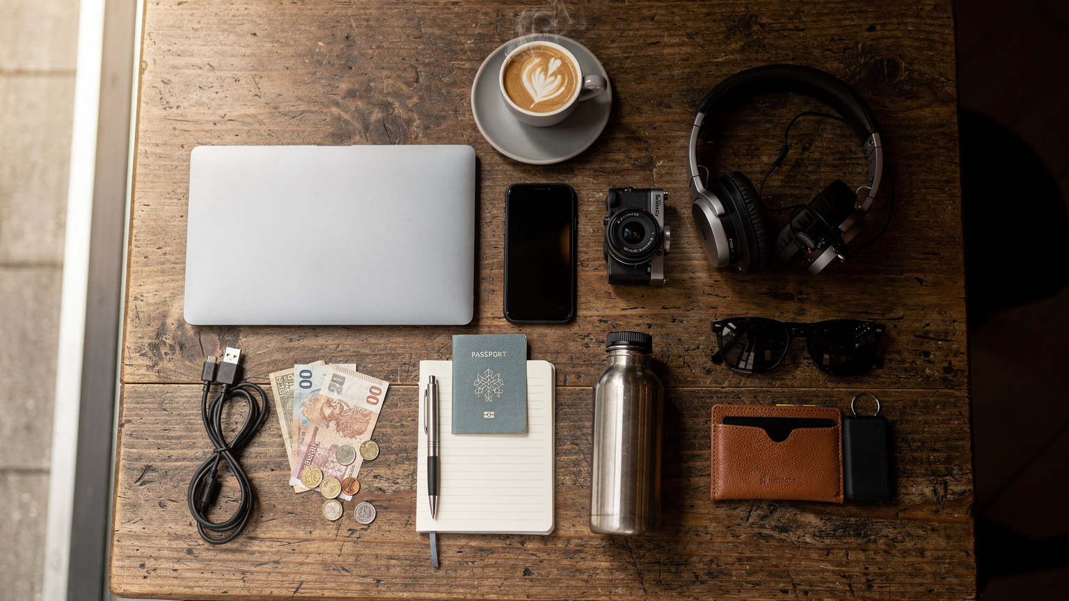 Ein Overhead-Flat-Lay-Shot auf einem Holztisch zeigt ein Smartphone, eine digitale Reiseroute auf einem Tablet, einen Reisepass, Kopfhörer und eine Tasse Kaffee, die eine organisierte Reiseplanung symbolisieren.