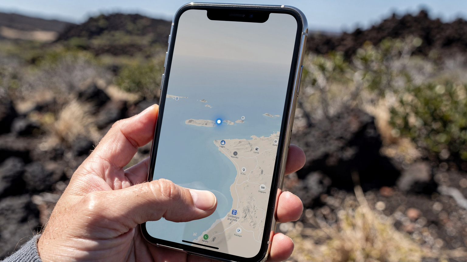 Nahaufnahme eines Smartphones mit einer angezeigten Karte, die einen kleinen Kreis um den Standort des Benutzers in einer abgelegenen Gegend der Galápagos-Inseln zeigt, während eine Hand versucht, das Gerät besser auszurichten.