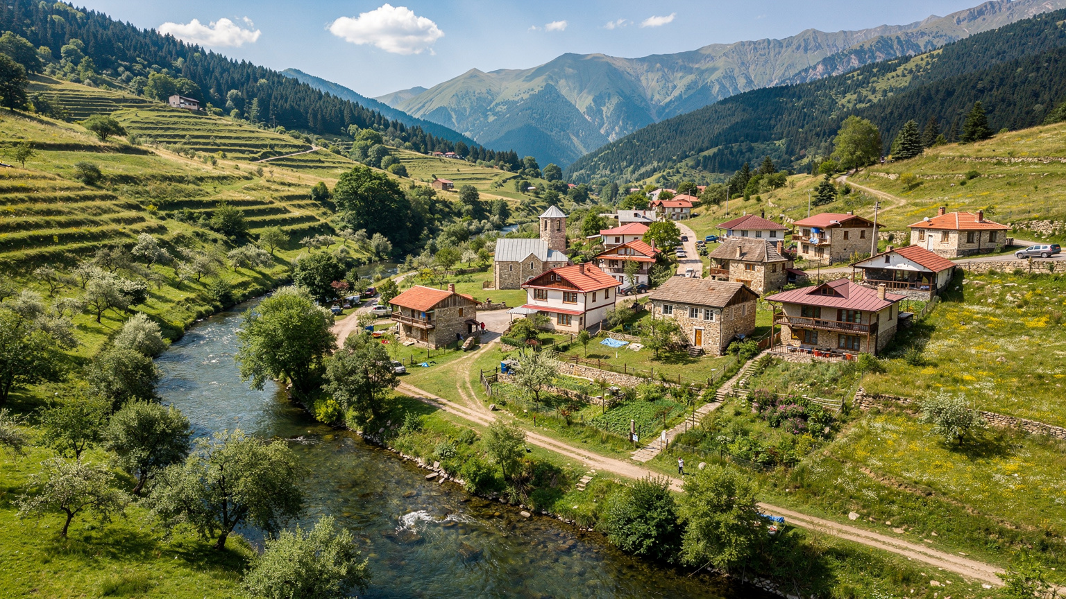 An aerial view of a picturesque Georgian village nestled in a valley with rolling hills and a winding river, emphasizing the blend of remote beauty and the need for connectivity even outside urban centers.