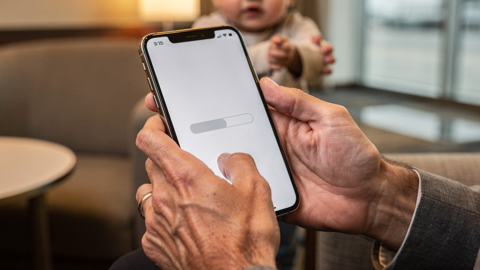 A close-up of a parent's hands carefully holding a smartphone with a partially downloaded eSIM profile, showing a subtle progress bar, while a child's hand playfully tugs at their sleeve in the background.