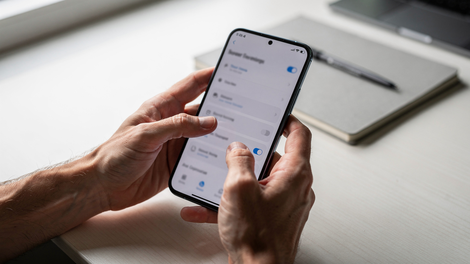 A close-up of a traveller's hands holding an Android phone, navigating through the settings menu to find the eSIM number, with the screen slightly out of focus to avoid showing UI text.