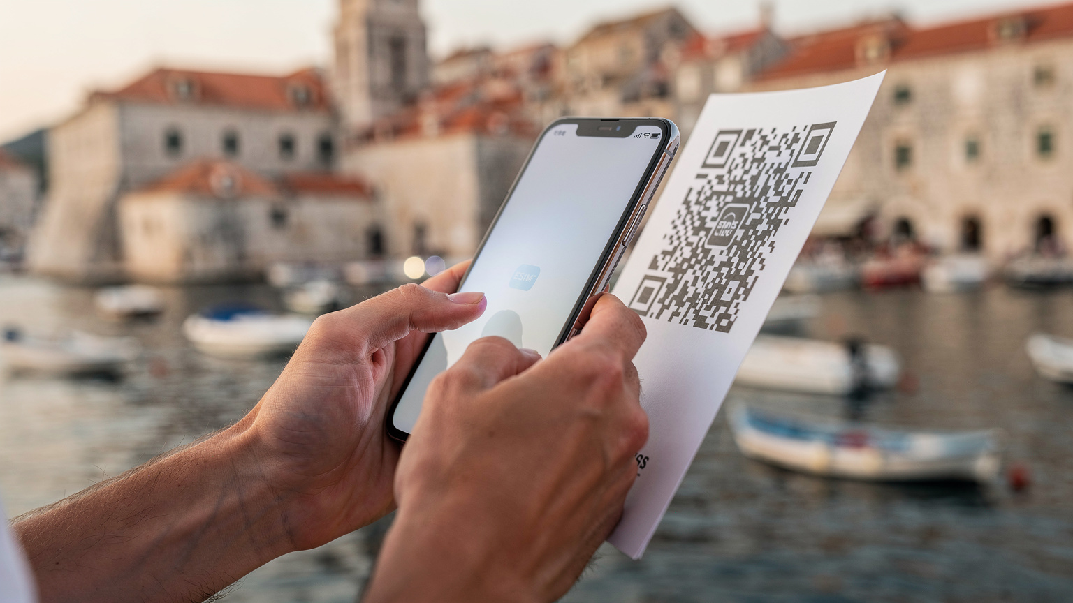 Närbild på ett par händer som håller en smartphone och skannar en QR-kod för att aktivera ett eSIM, med en pittoresk kroatisk hamnstad som Dubrovnik i oskarp bakgrund.