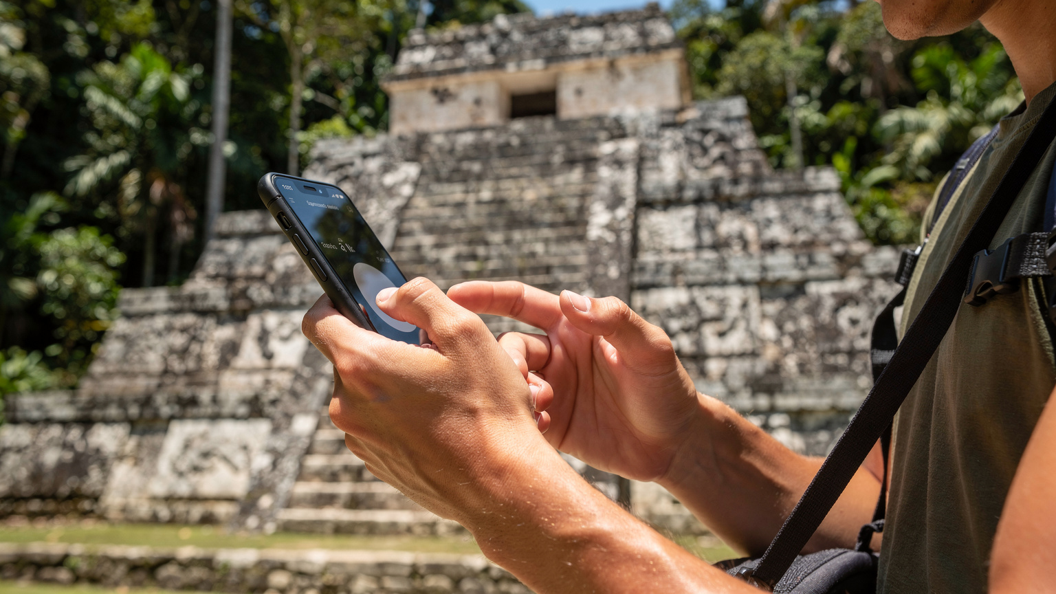 Meksika'nın Palenque antik kentindeki bir Maya tapınağının önünde, genç bir gezginin akıllı telefonunda bir çeviri uygulamasını kullandığı yakın çekim fotoğrafı.