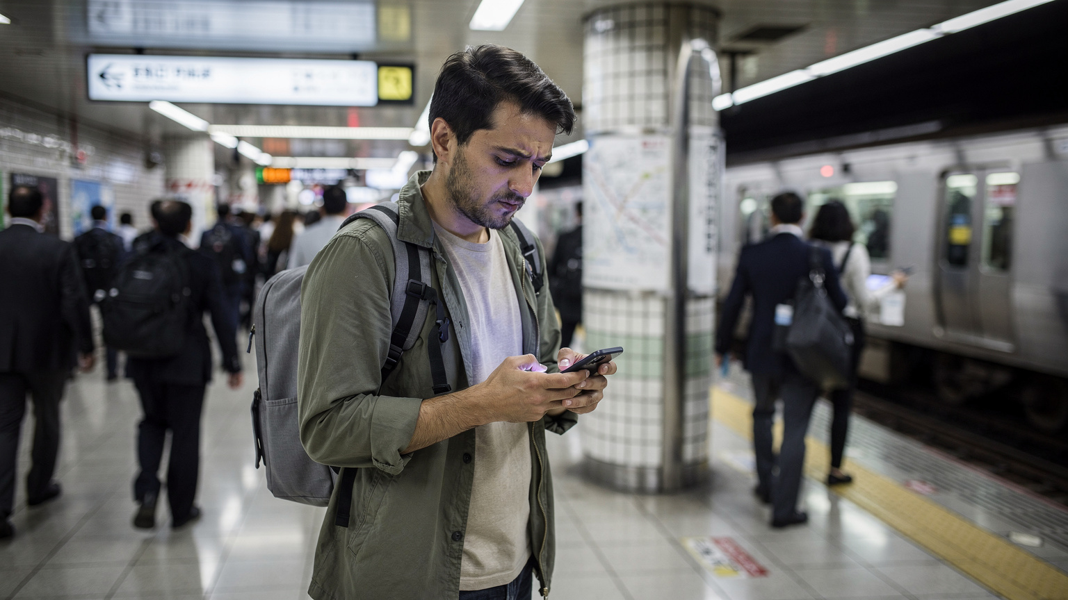 一個旅行者在東京地鐵站的月台上,低頭看著手機,屏幕上顯示著「無服務」的提示,表情略顯焦慮,背景是繁忙的日本鐵路系統。