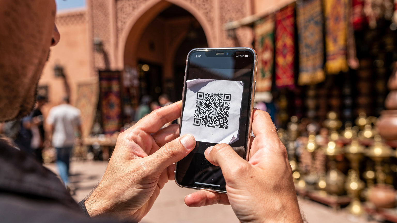 Ein Reisender in einem traditionellen marokkanischen Souk in Marrakesch hält ein Smartphone und scannt einen QR-Code auf einem ausgedruckten Blatt Papier, um eine eSIM zu aktivieren.