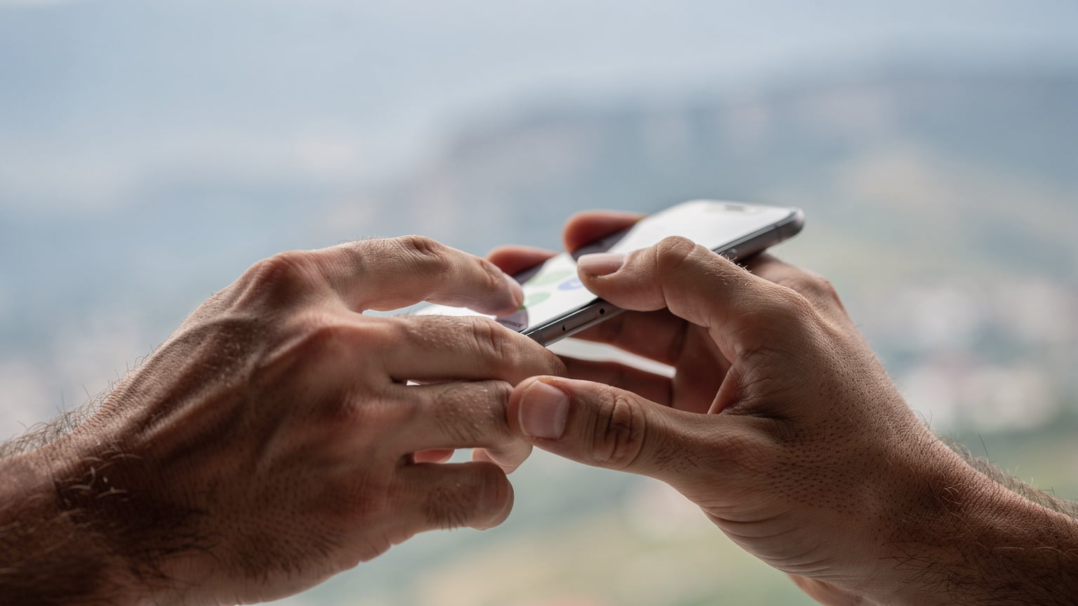 Detailní záběr rukou cestovatele, který v ruce drží smartphone s aktivovanou eSIM, na pozadí je rozmazaná mapa Albánie.